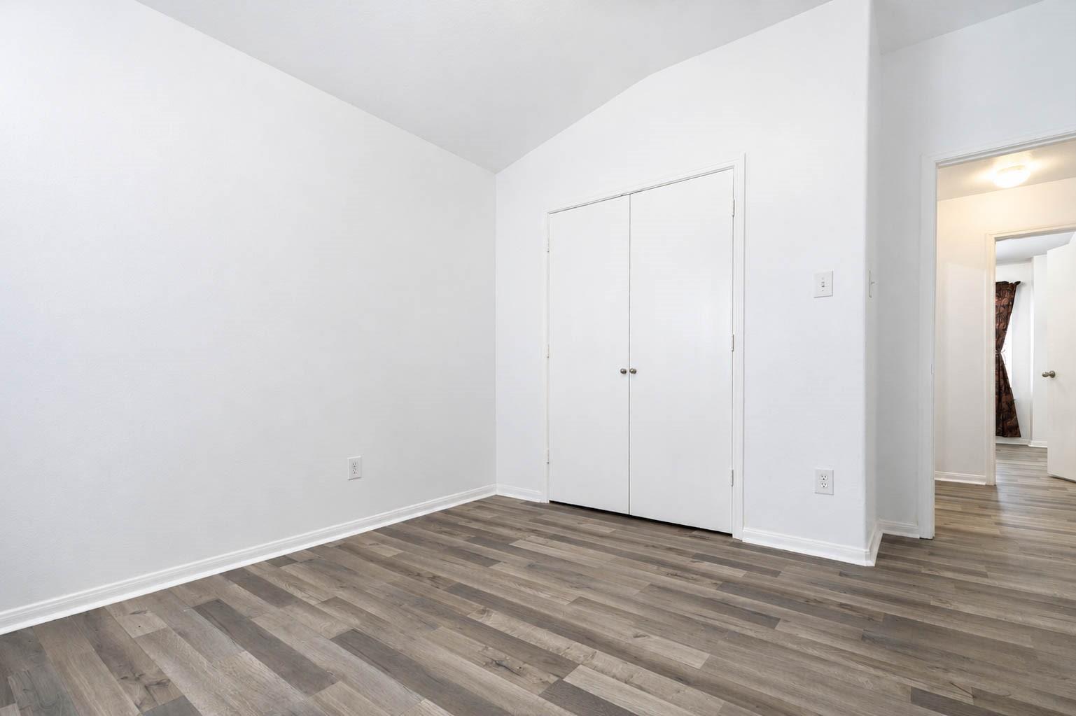 Empty room with gray-brown plank flooring, a double-door closet, and an open doorway to the hall.