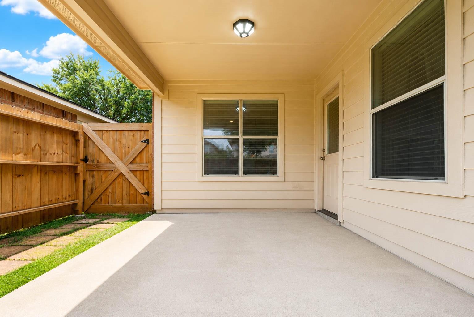Covered concrete patio with a wooden privacy fence and gate beside the house.