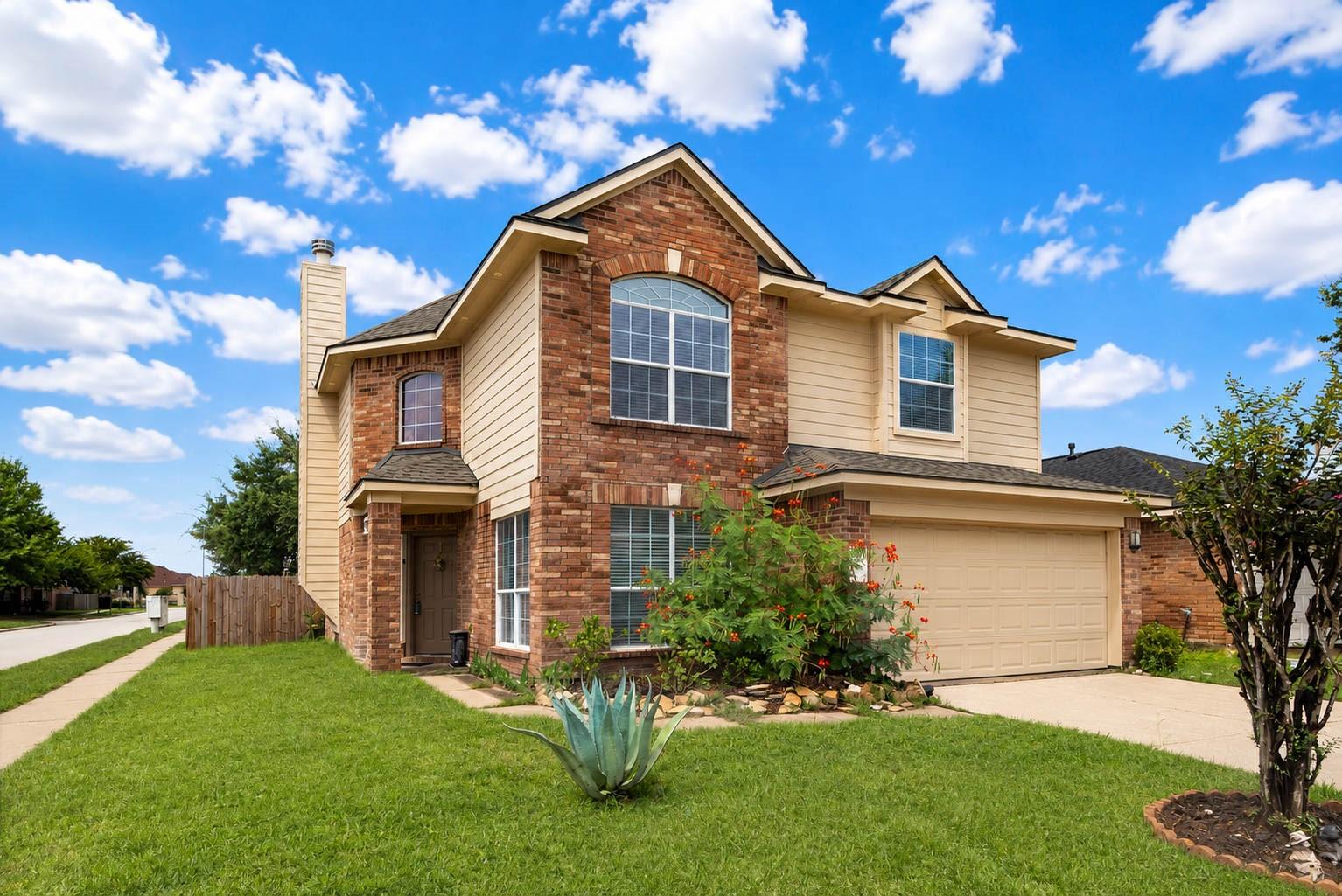 Two-story brick-and-beige house with an attached garage, arched window, and landscaped front lawn.