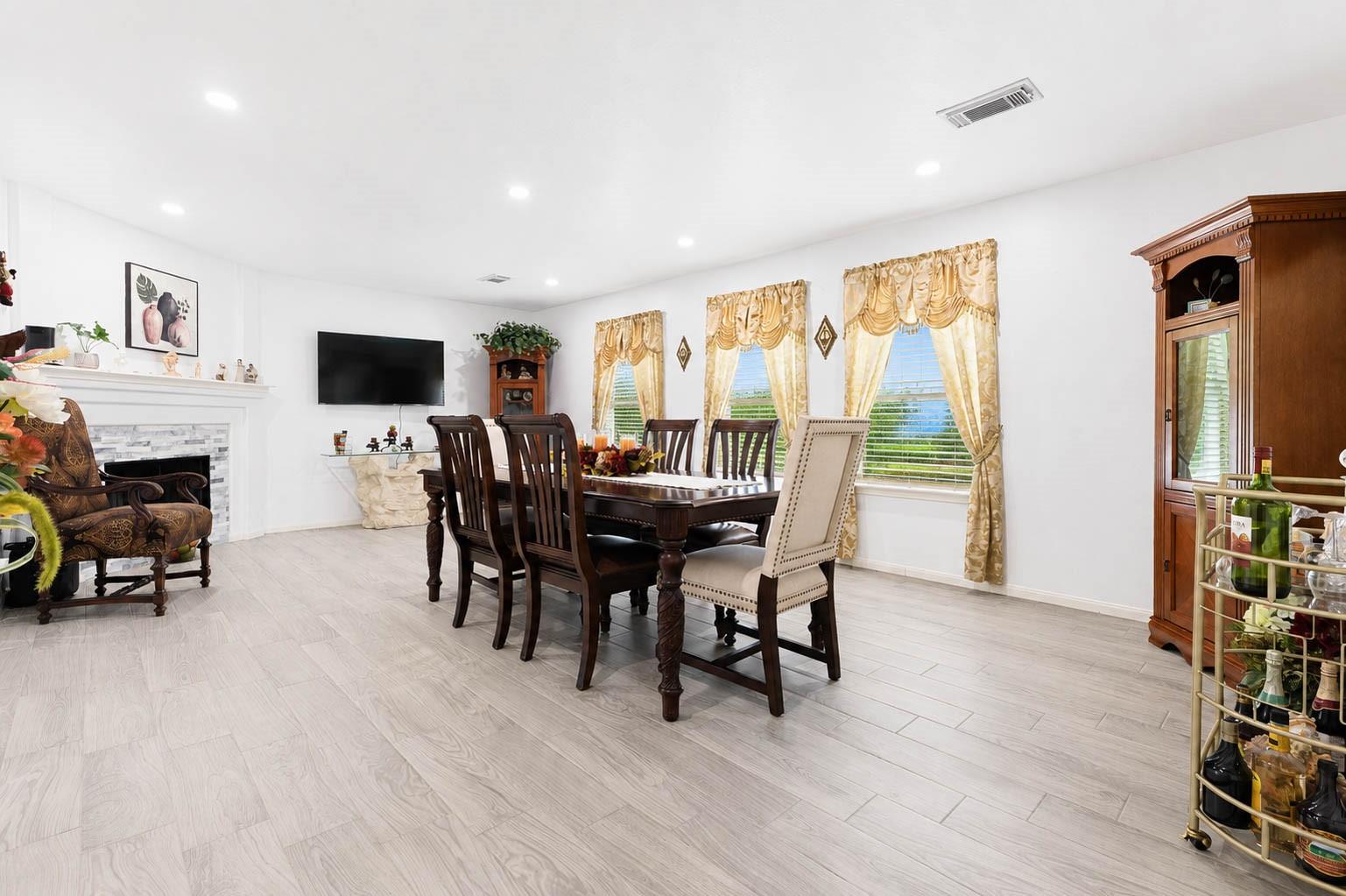 Furnished dining room with a dark wood table, white fireplace, and three curtained windows.