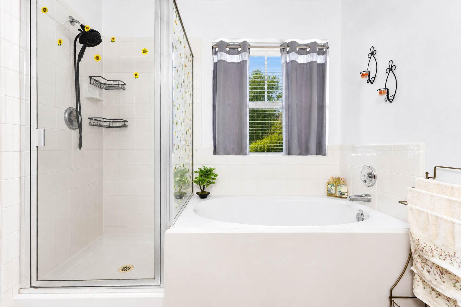 Bright bathroom with a glass-enclosed shower and large soaking tub beneath a window.