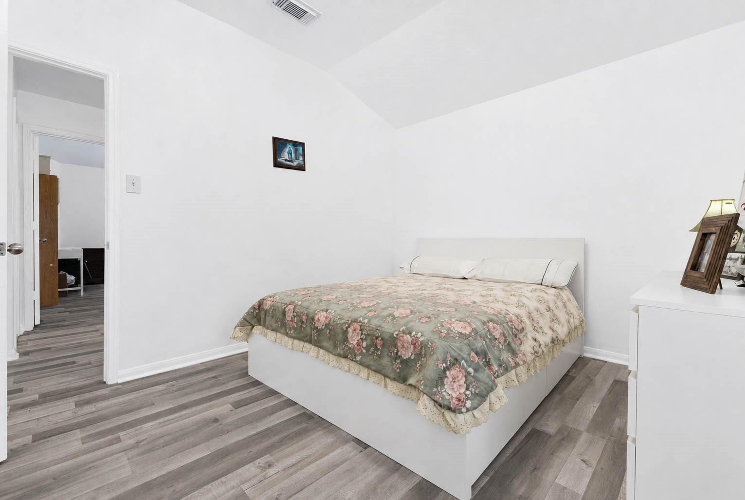 Bedroom with a white bed, floral comforter, and gray wood-look flooring.