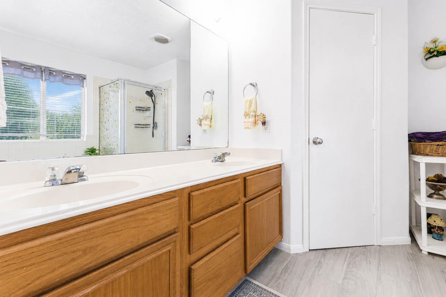 Bathroom with a double-sink wood vanity and glass-enclosed shower beside a window.