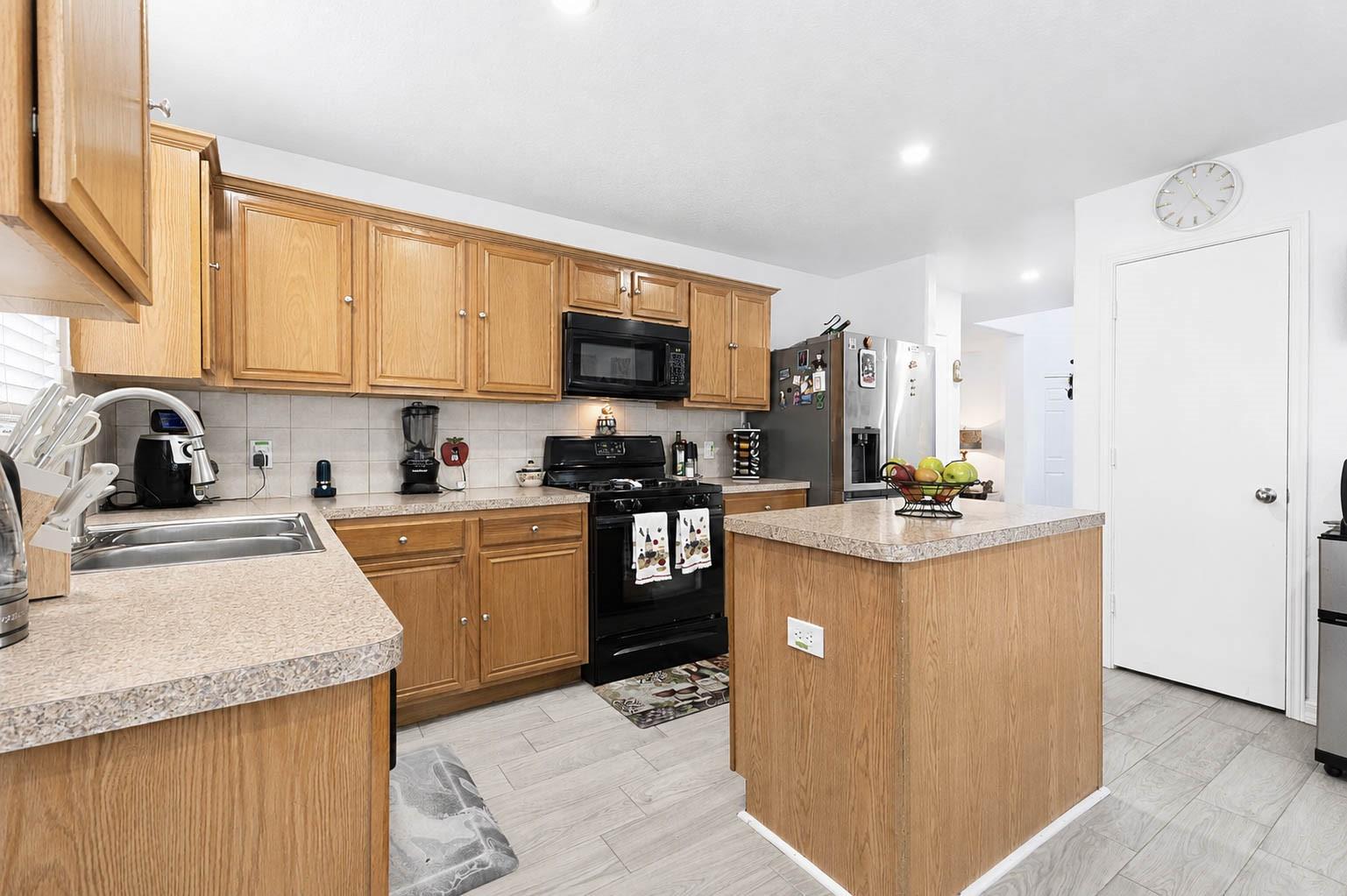 Kitchen with honey-colored wood cabinets, a central island, and black appliances.