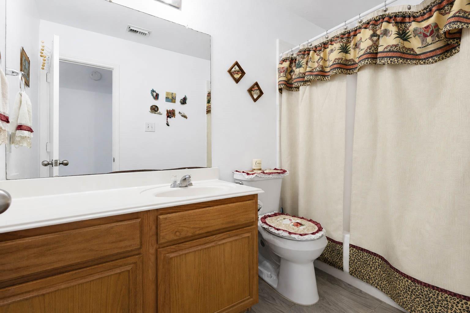 Bathroom with a wood vanity, large mirror, and patterned shower curtain.