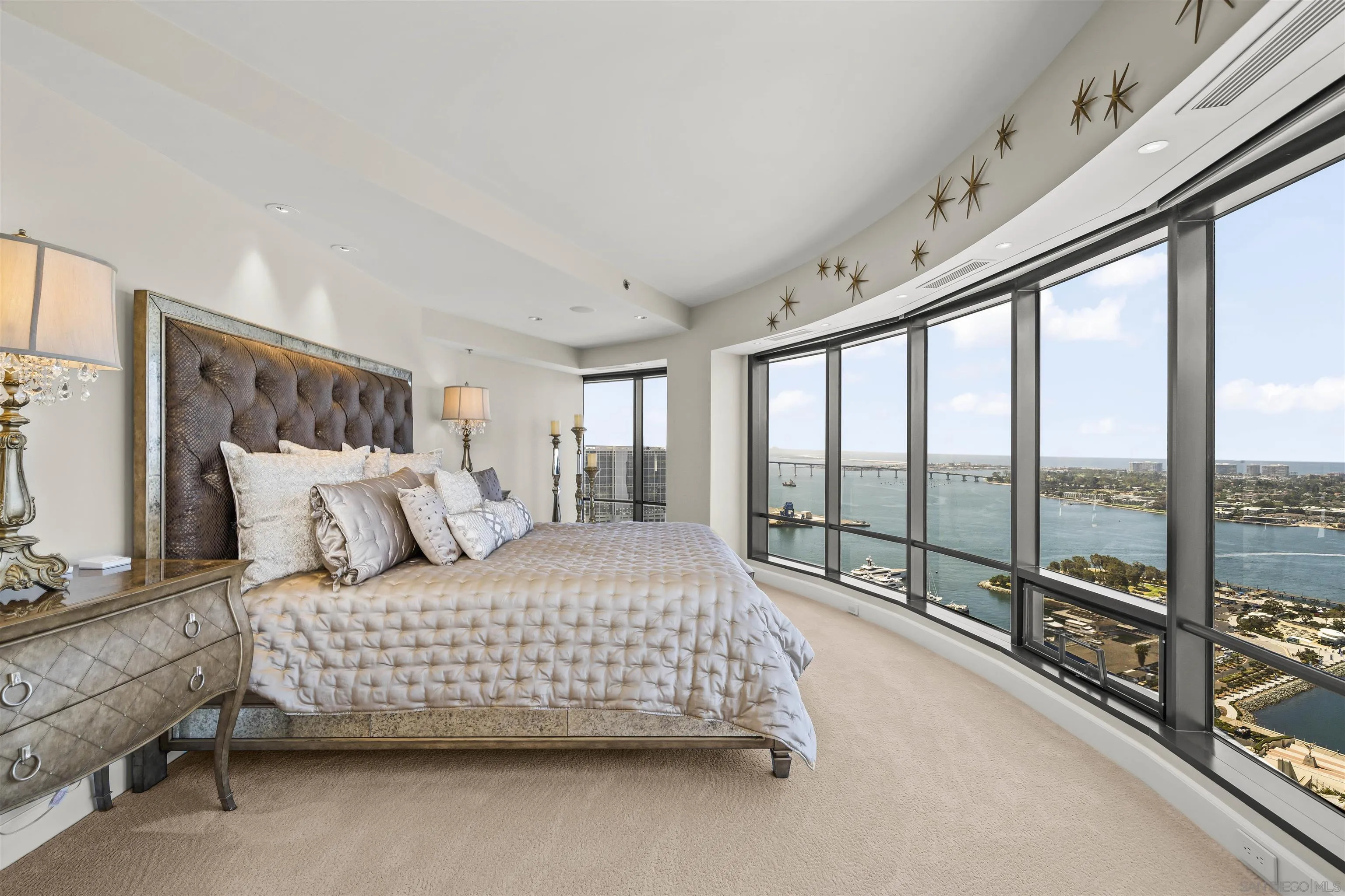 High-rise bedroom with tufted headboard and floor-to-ceiling bay-view windows.