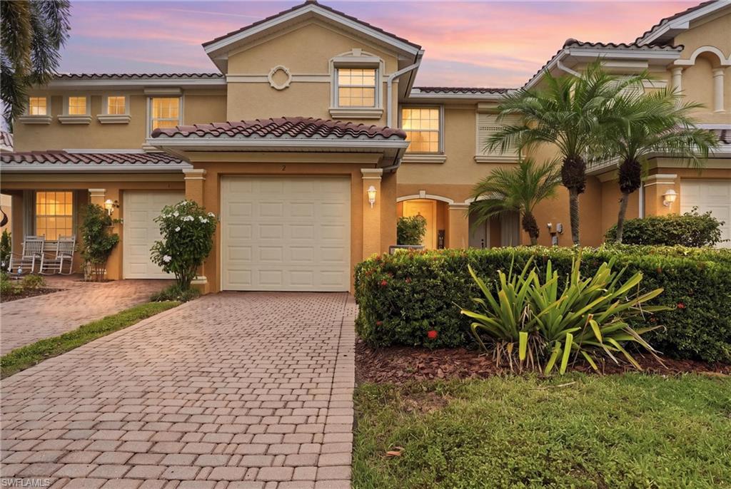 Two-story stucco home with a paver driveway, tiled roof, and palm-lined landscaping at dusk.