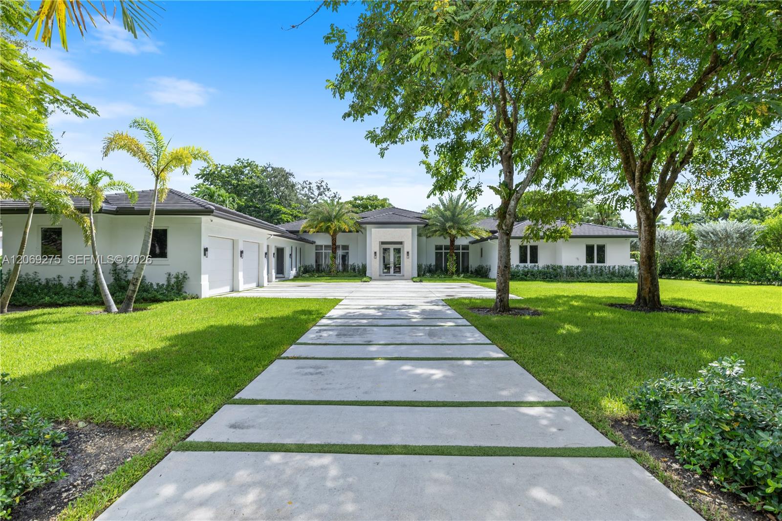 Modern white single-story home with a wide concrete driveway and tropical landscaping.