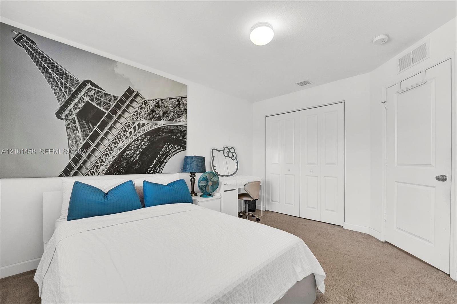 Furnished bedroom with blue pillows, an Eiffel Tower mural, and white closet doors.