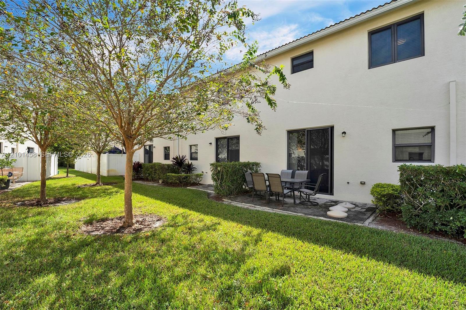 Two-story home with a paved patio and outdoor dining set beside a leafy lawn.