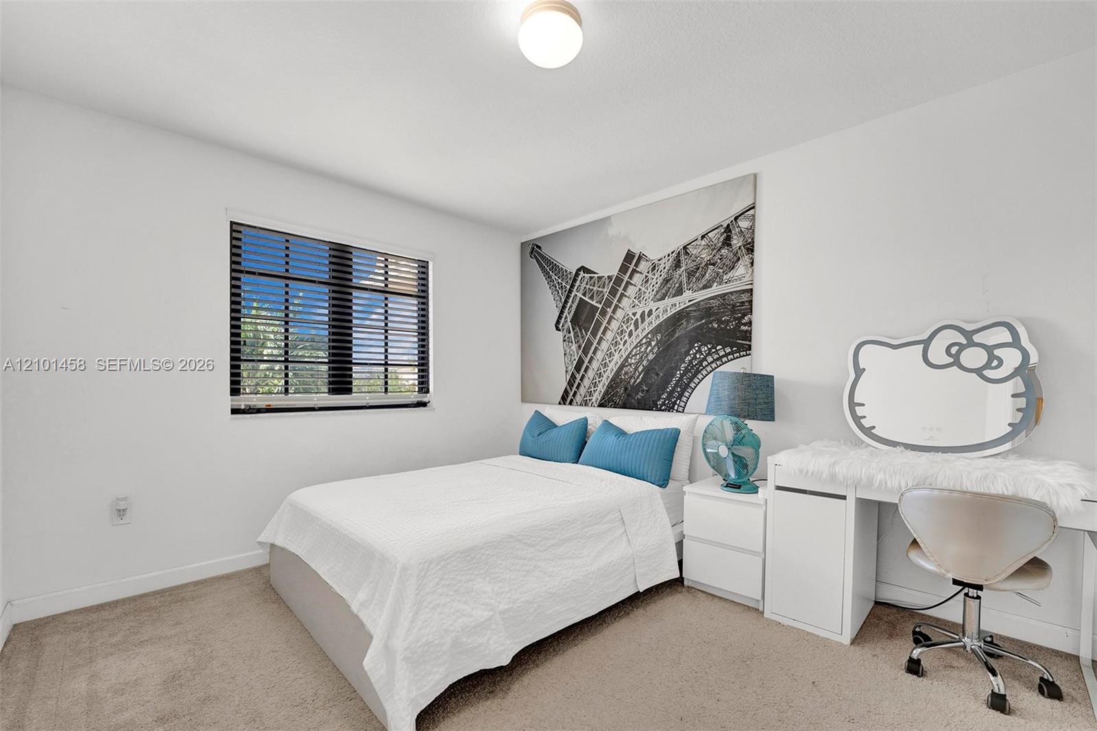 Bedroom with a white bed, turquoise pillows, Eiffel Tower print, and desk with a Hello Kitty-shaped mirror.
