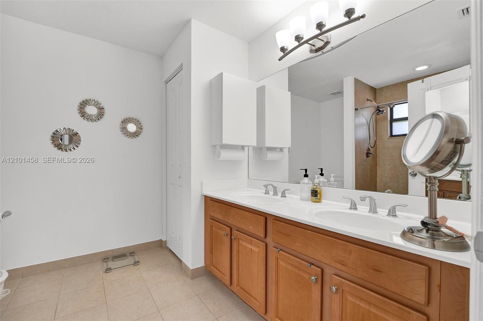 Bathroom with a long double-sink vanity, wood cabinets, mirrored cabinets, and a tiled shower.
