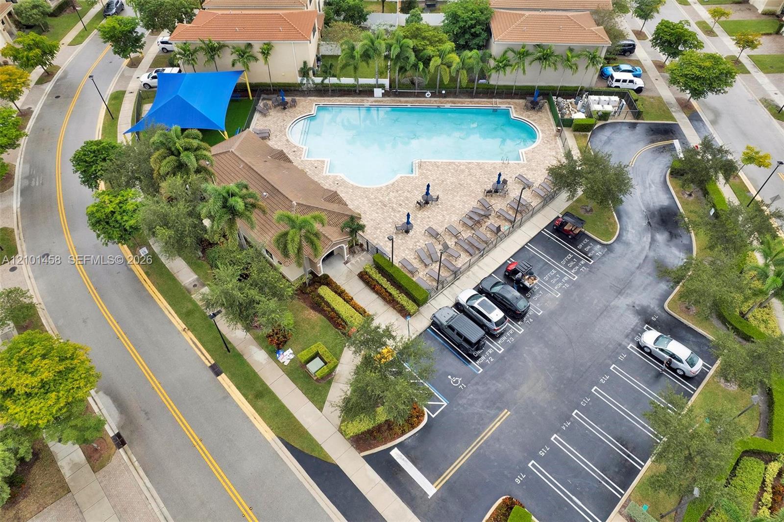 Aerial view of a community pool with a blue shade canopy and surrounding lounge deck.