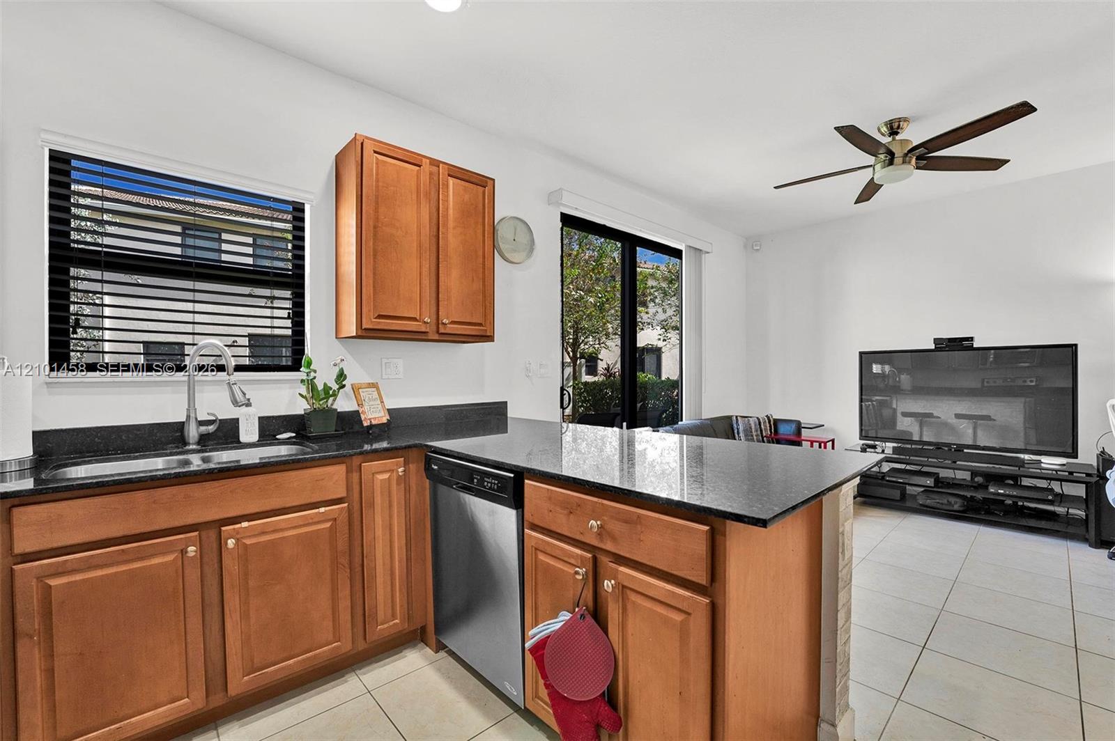 Kitchen with warm wood cabinets and dark countertops opening into a living area.