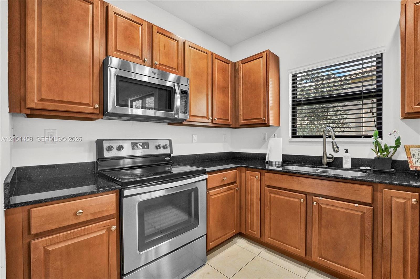 Kitchen with honey-colored cabinets, black countertops, stainless steel appliances, and a window over the sink.