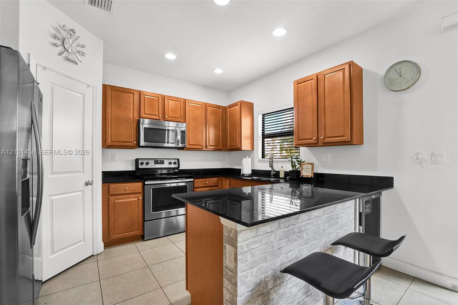 Kitchen with wood cabinets, stainless steel appliances, and a stone-faced island with two bar stools.