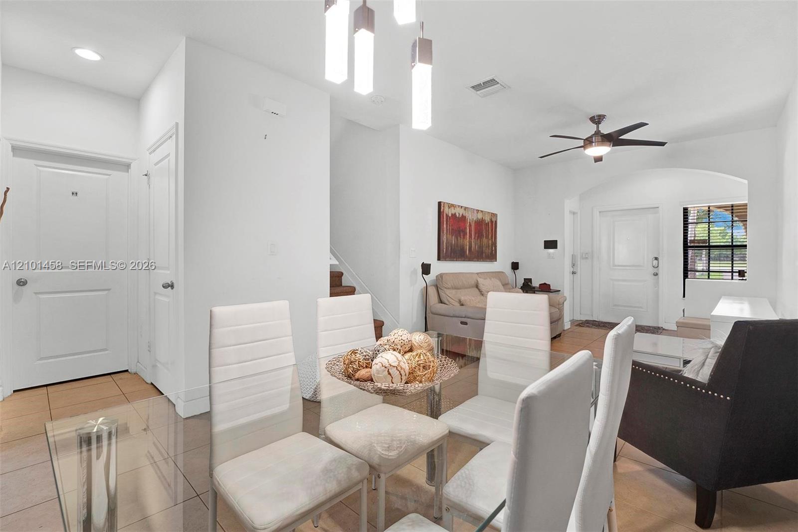 Open living and dining area with glass table, white chairs, and beige sofa beneath abstract art.