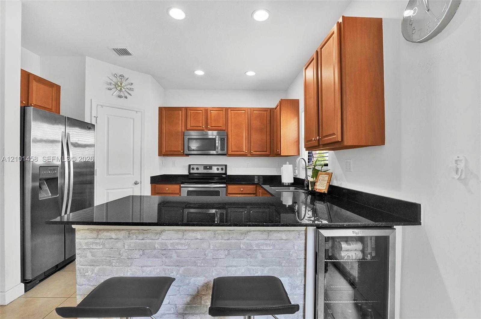 Kitchen with wood cabinets, black granite counters, stainless appliances, and a stone-faced breakfast bar.