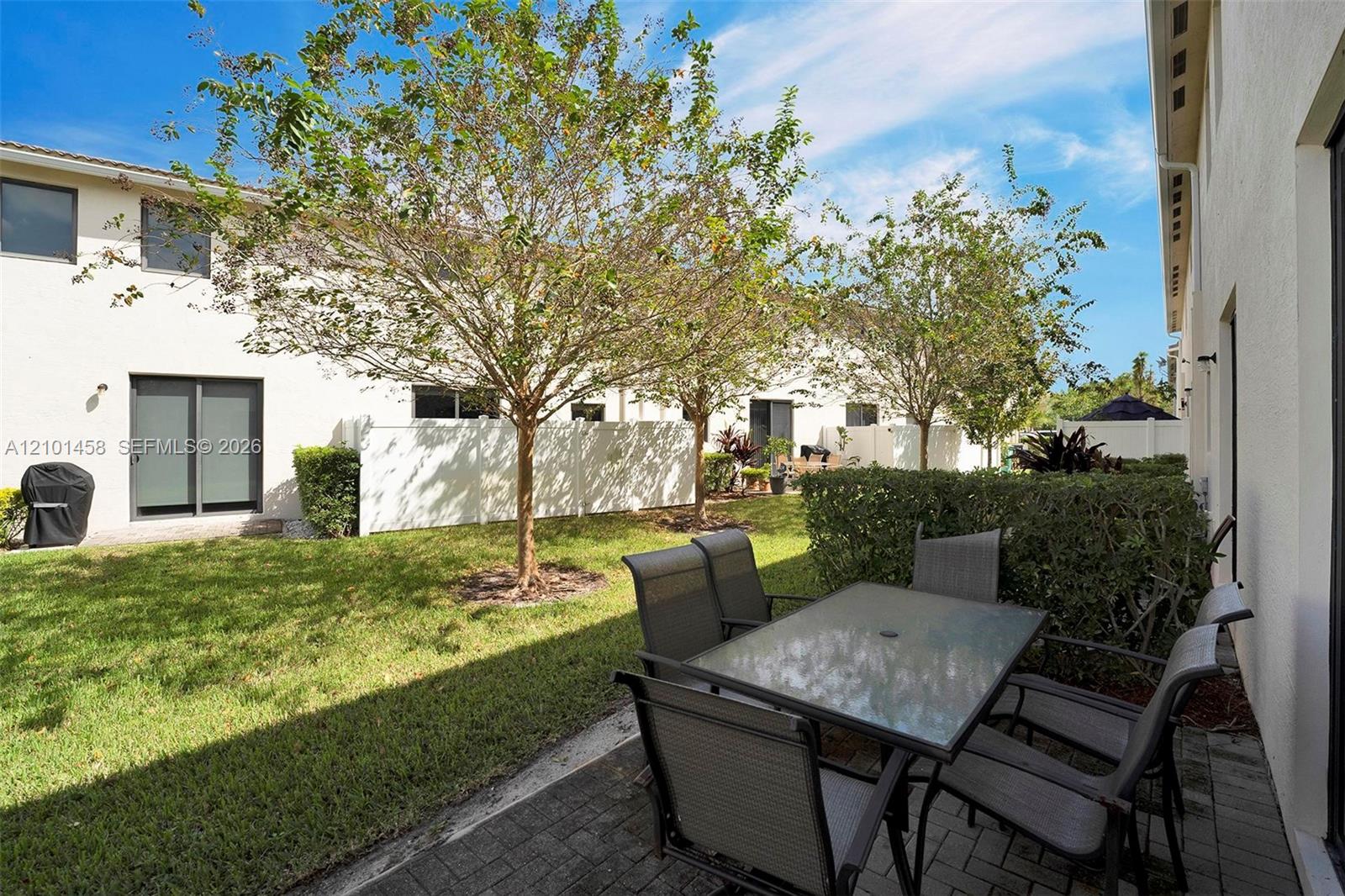 Townhouse courtyard patio with outdoor dining furniture, a lawn, trees, and white privacy fencing.