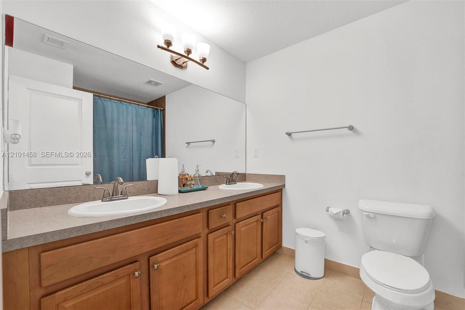 Bathroom with a long wood vanity, double sinks, large mirror, and blue shower curtain.