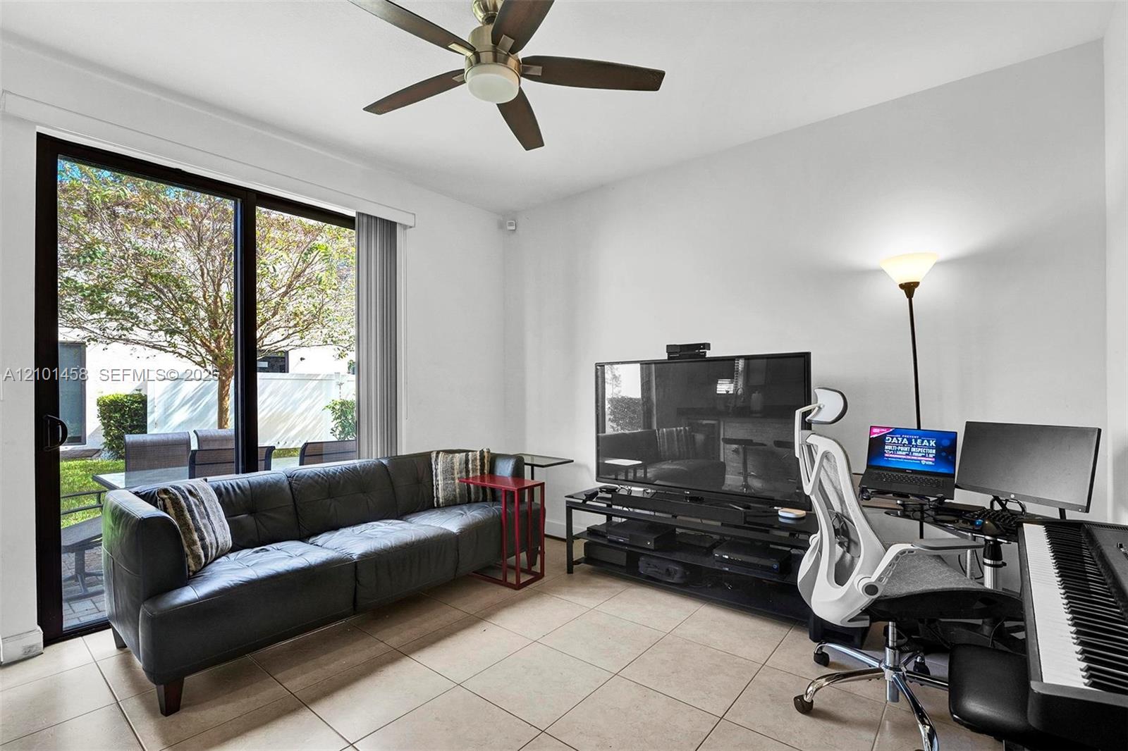 Living room with a black leather sofa, patio-facing sliding doors, and a desk setup.