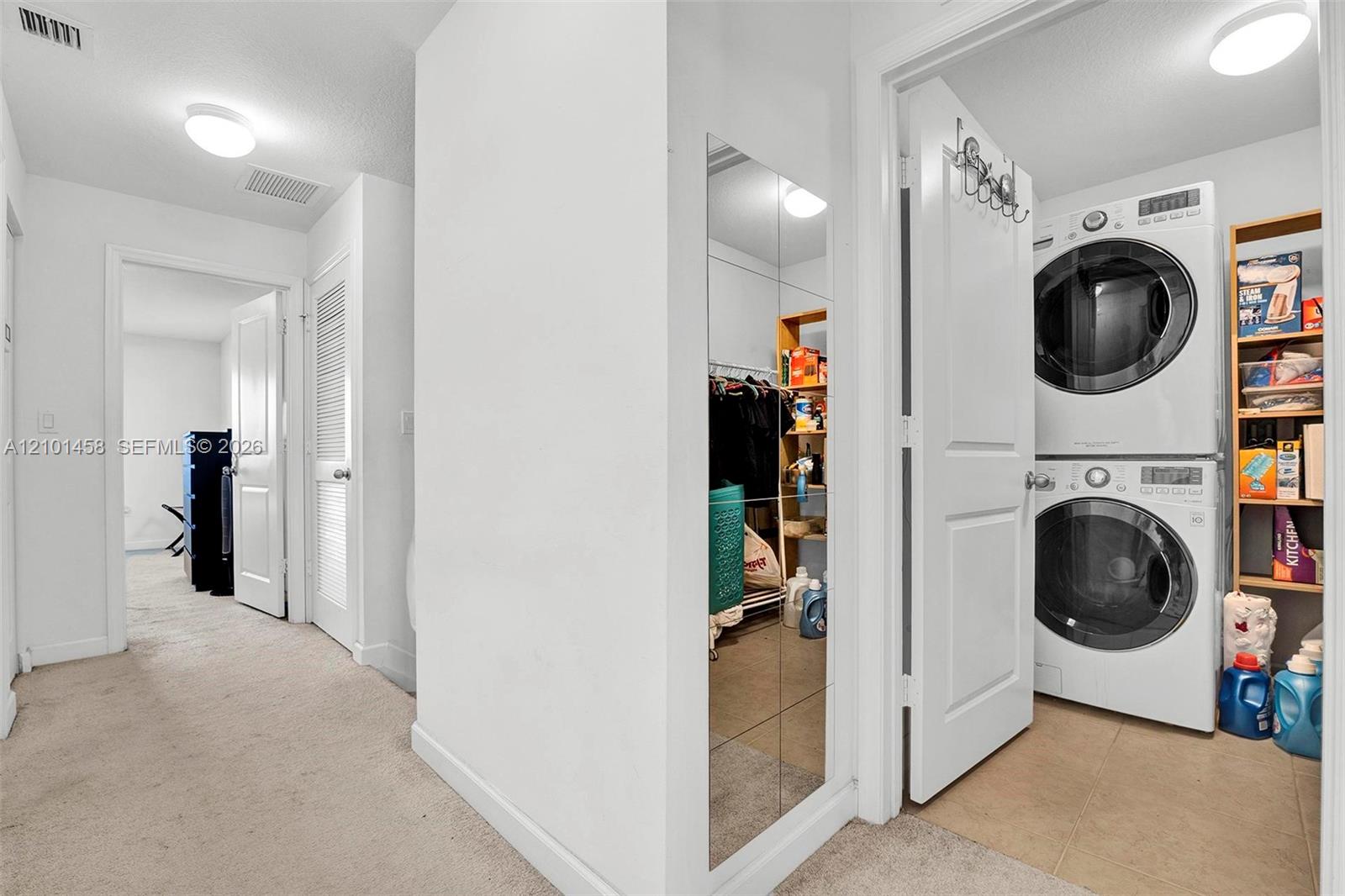 Laundry area with stacked washer and dryer beside open storage shelves and a mirrored closet.