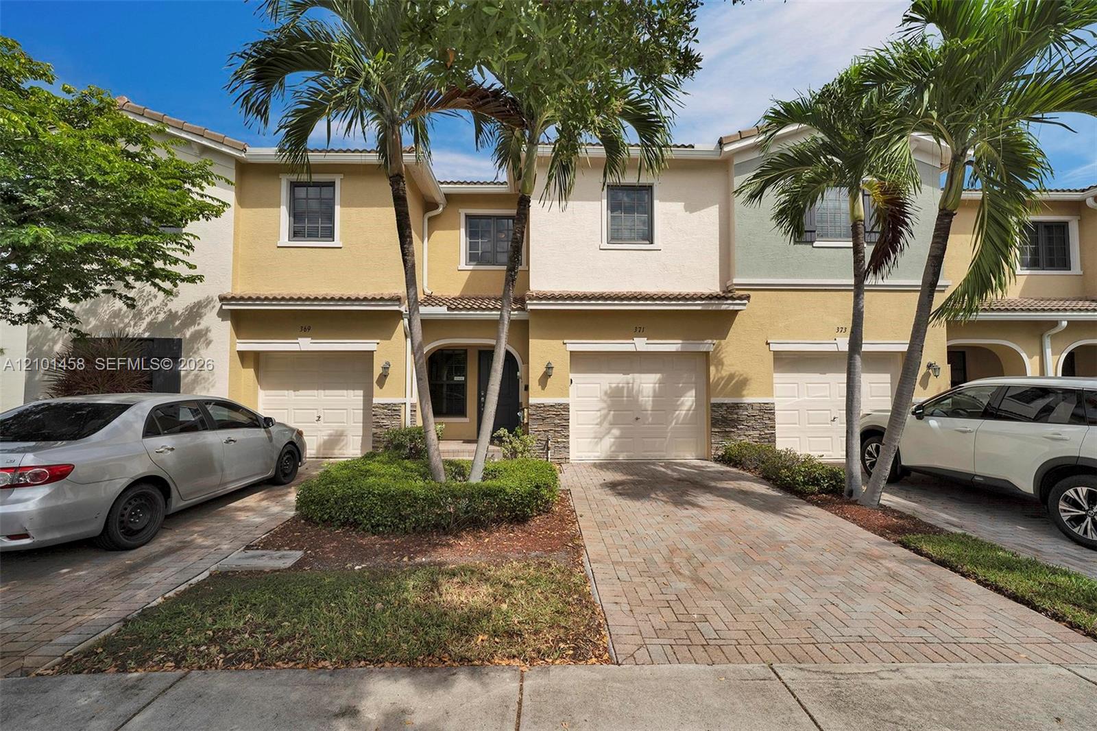 Townhome numbered 371 with an attached garage, brick-paver driveway, and palm trees.