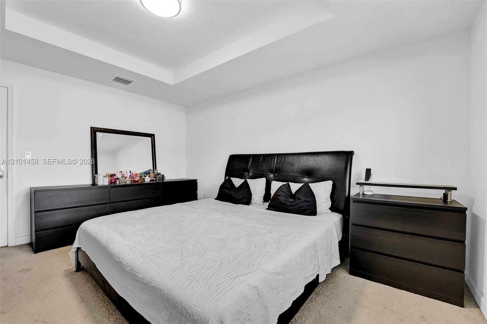 Bedroom with a black leather headboard, white bedding, and dark wood dressers.
