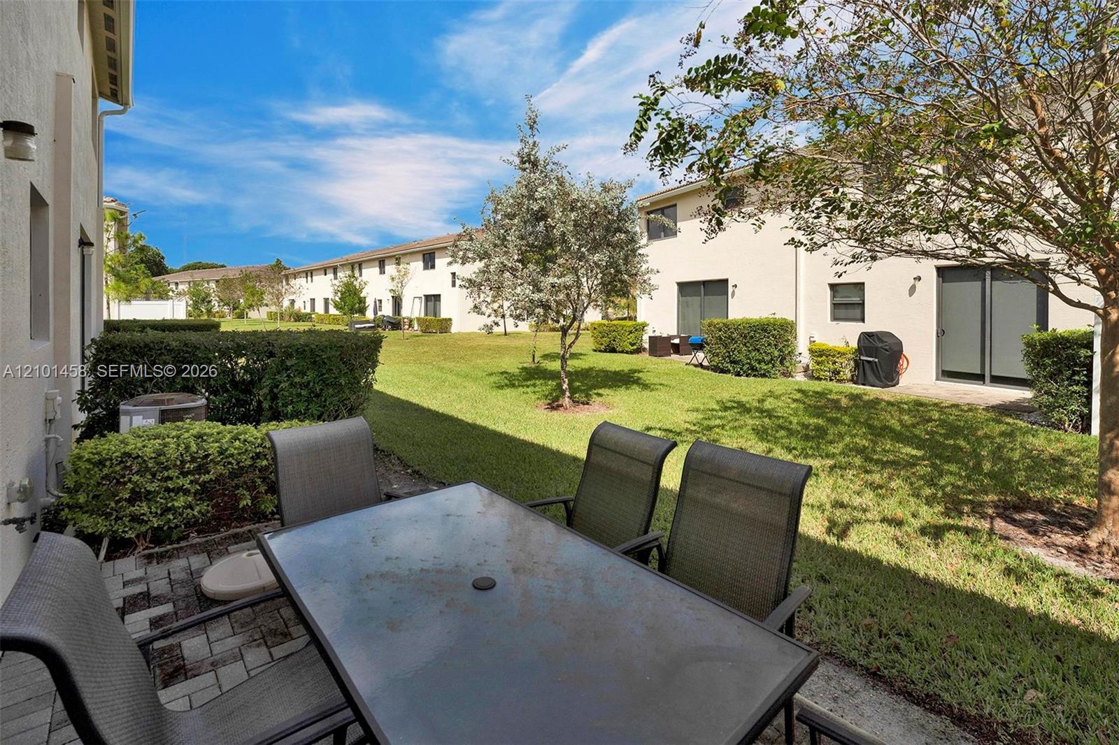 Patio with outdoor dining furniture overlooking a grassy courtyard and neighboring two-story residences.