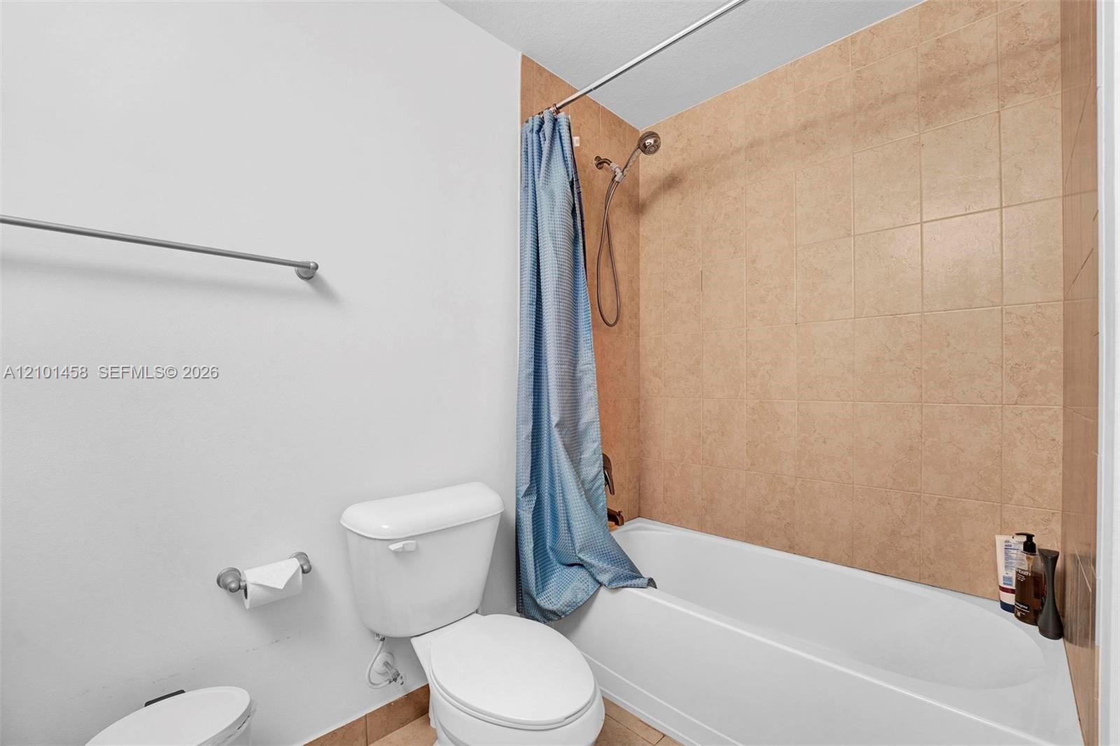 Bathroom with a tan tiled tub surround and blue shower curtain.