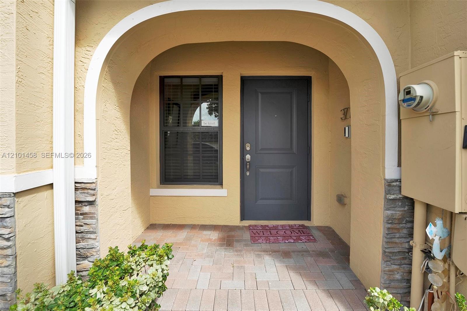 Arched home entry with a dark gray door, tiled walkway, and welcome mat.