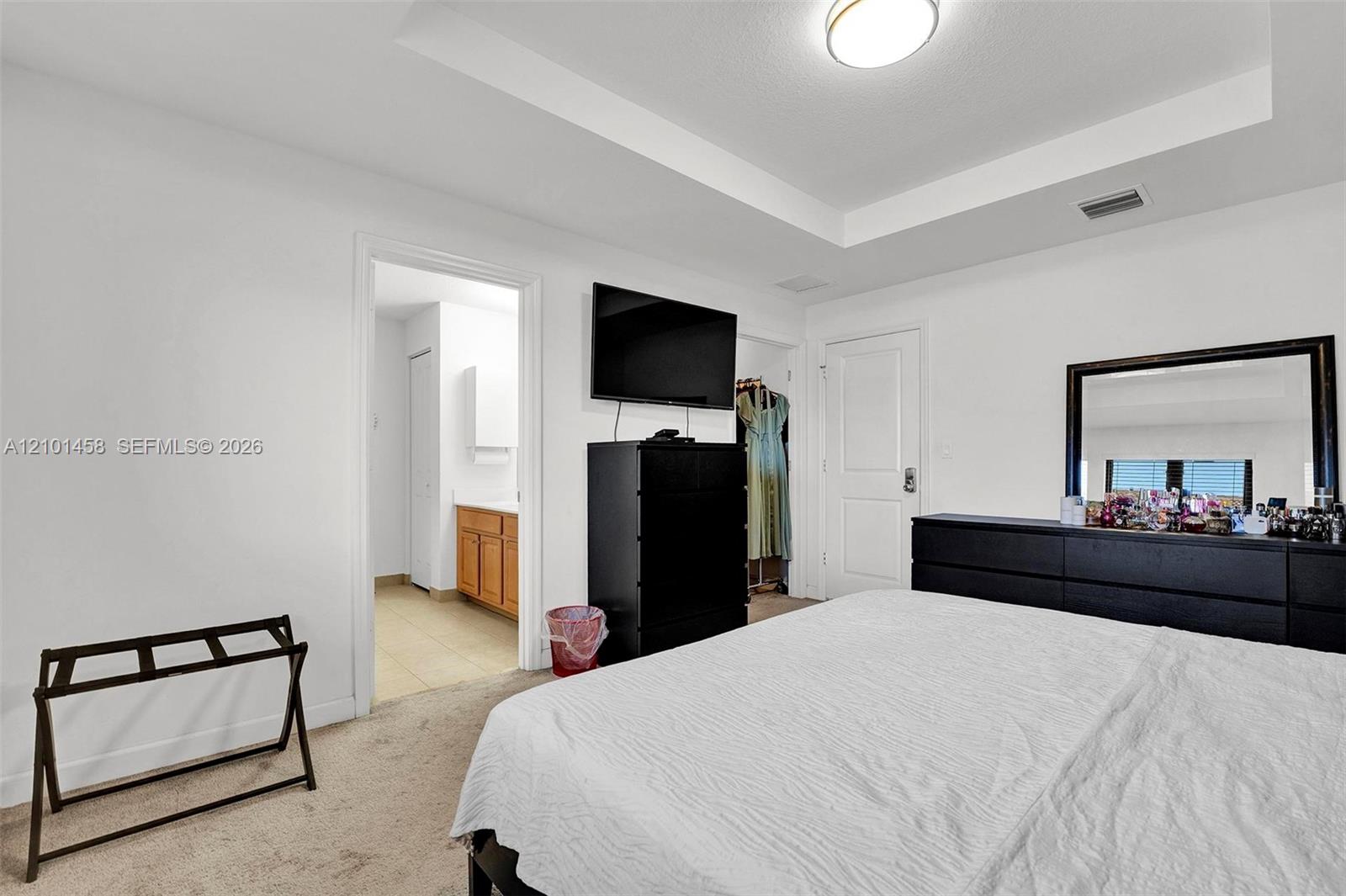 Bedroom with a large bed, black dresser and TV, and an open doorway to a bathroom.