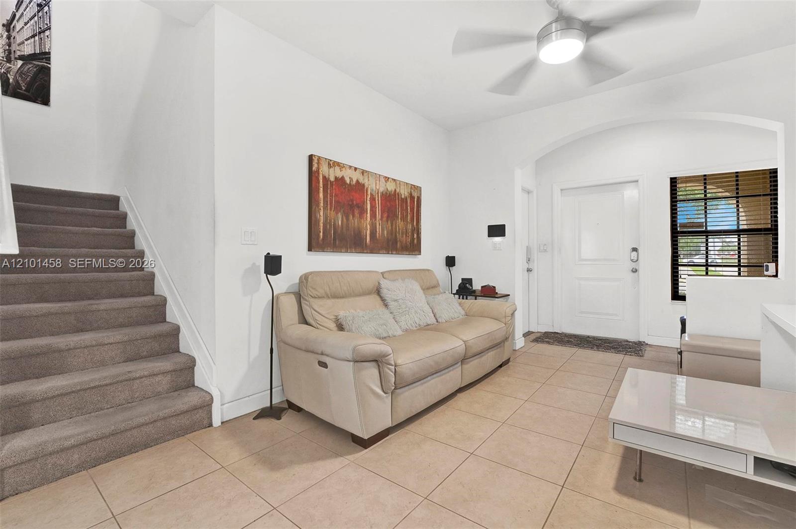 Living room with a cream sofa, tiled floor, and carpeted staircase beside the entry.