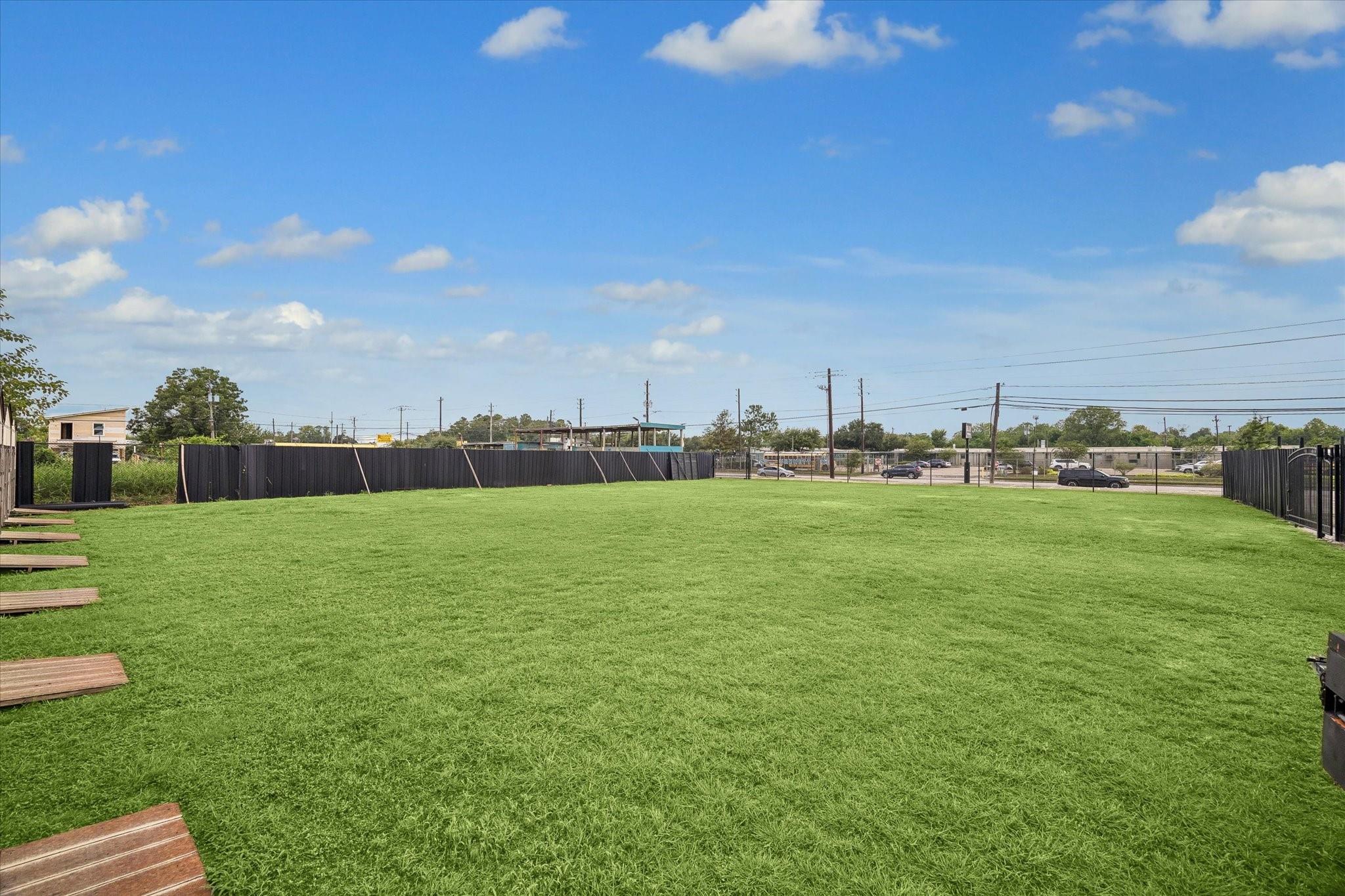 Fenced grassy lot with wooden platforms along one edge and a street beyond.