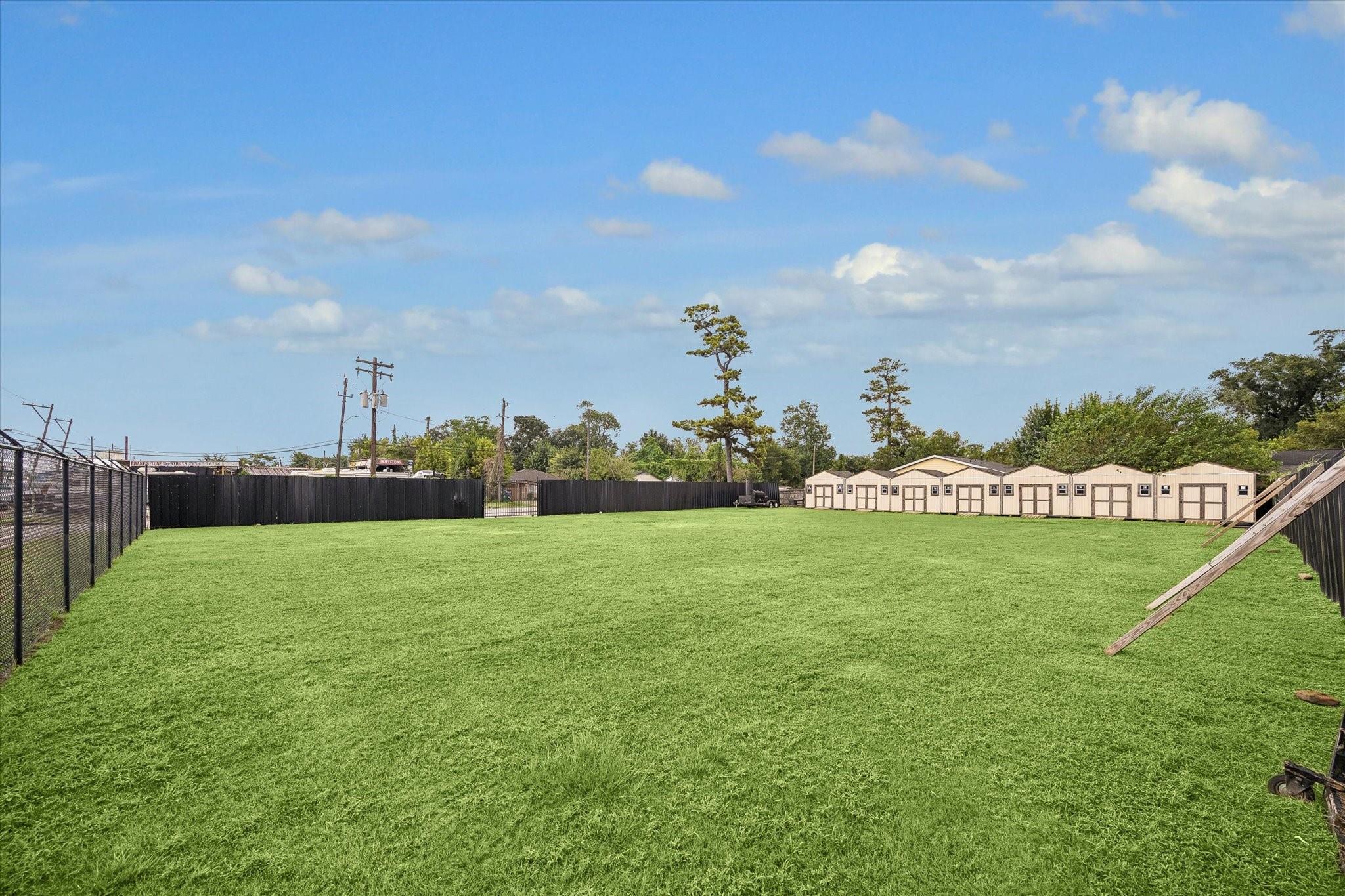 Fenced grassy lot with a row of beige storage buildings along the far side.