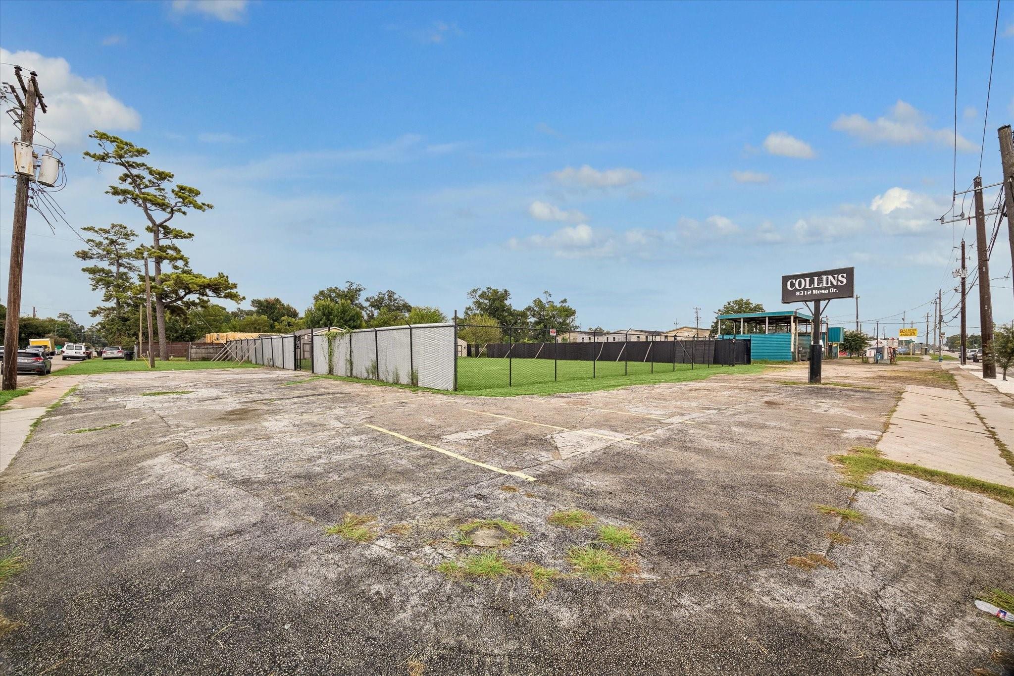 Commercial lot with cracked asphalt parking, a fenced grassy area, and a Collins sign.
