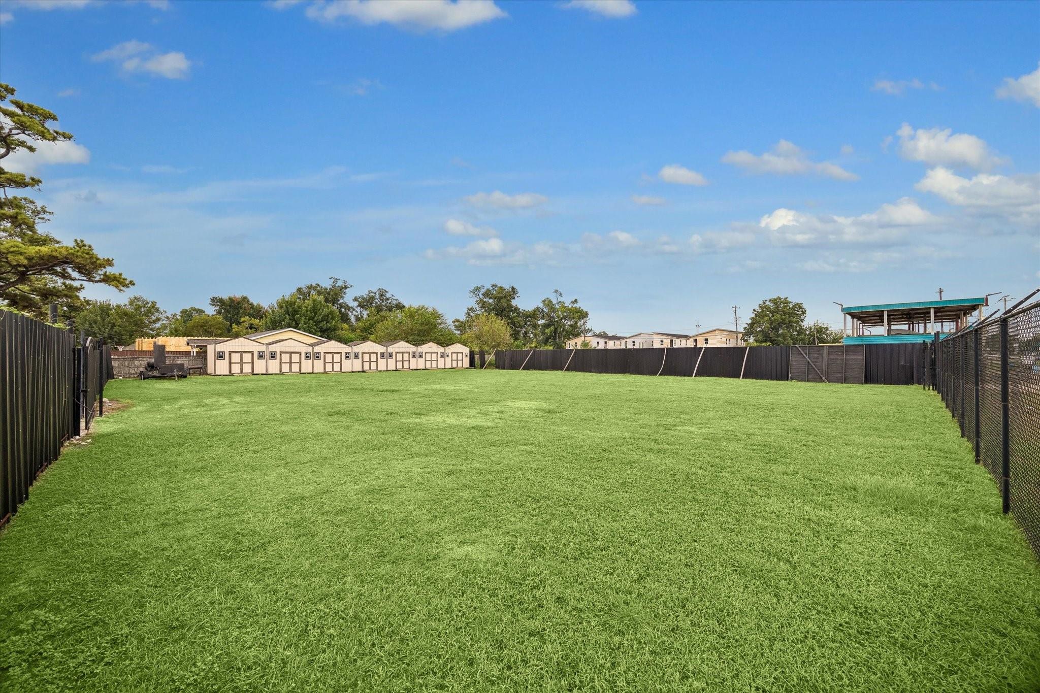 Fenced grassy yard with a row of beige storage sheds along the far side.