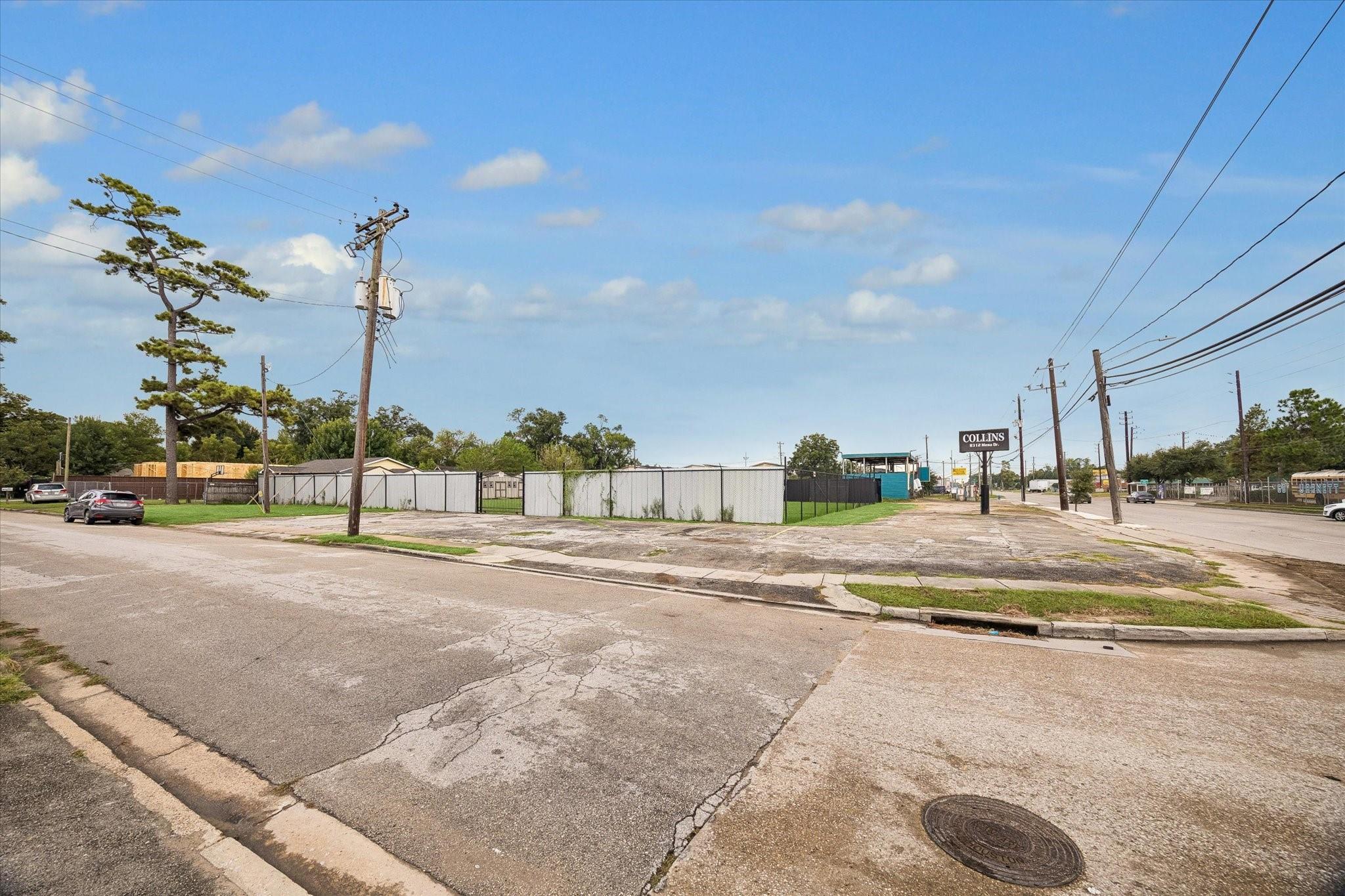 Fenced vacant corner lot with a broad cracked driveway and a roadside Collins sign.