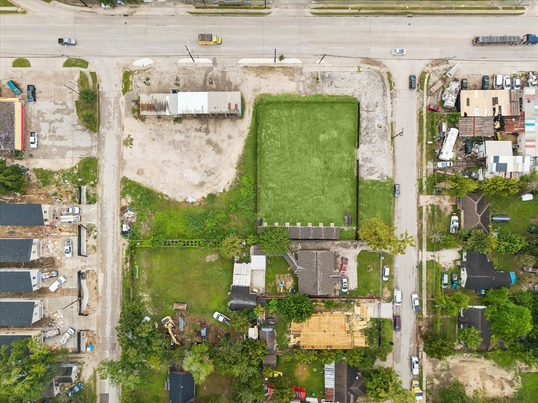 Aerial view of a property with a large fenced green area and adjoining cleared lot.