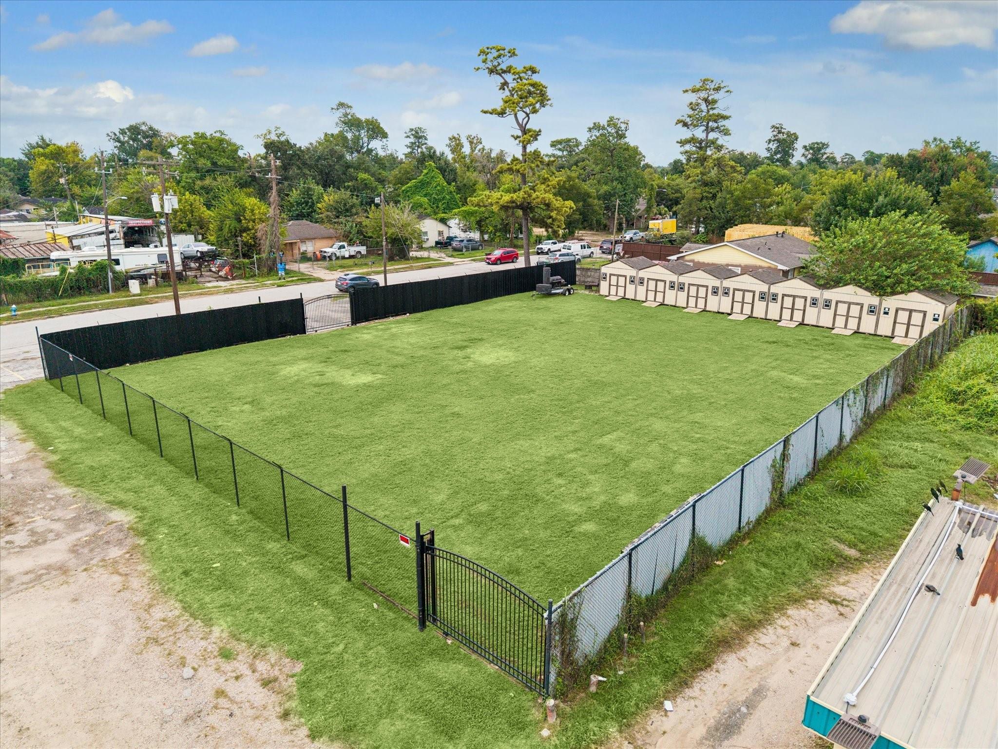 Aerial view of a fenced grassy lot with beige storage sheds along one side.