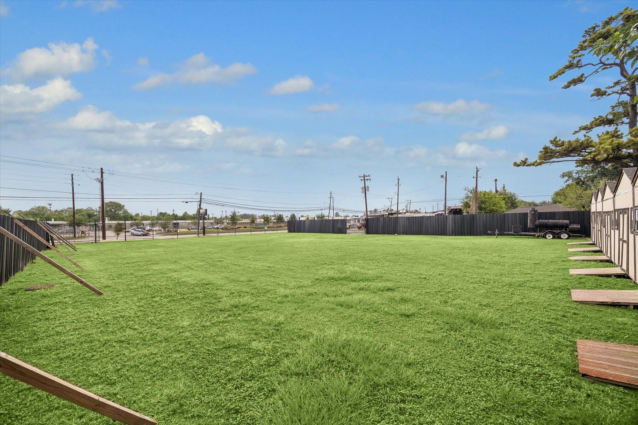 Fenced grassy yard beside a row of small buildings, with utility poles and power lines beyond the fence.