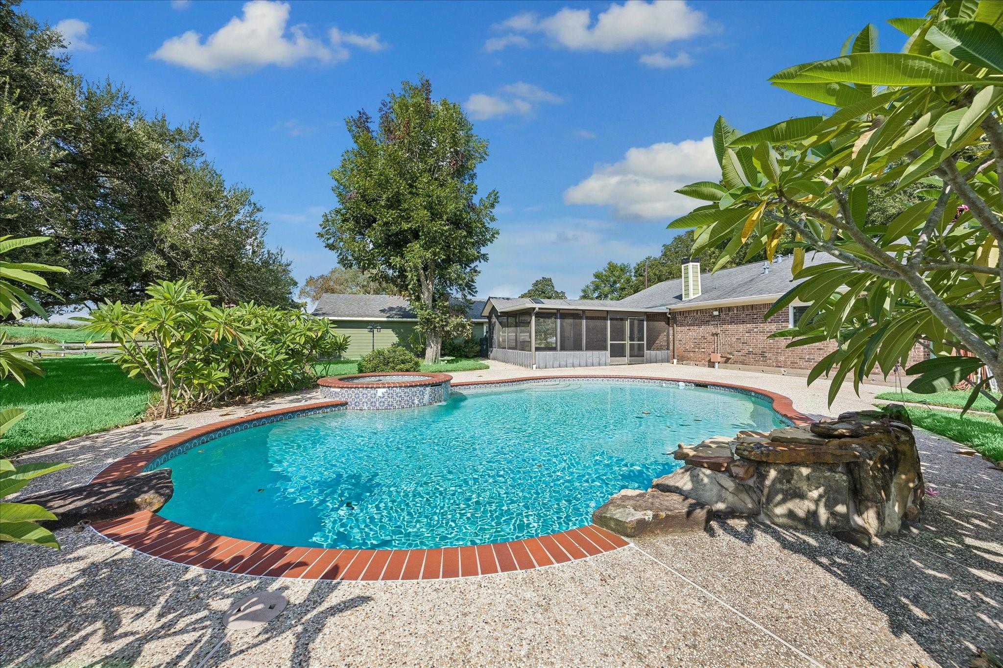 Backyard swimming pool with raised spa and rock waterfall beside a screened patio.