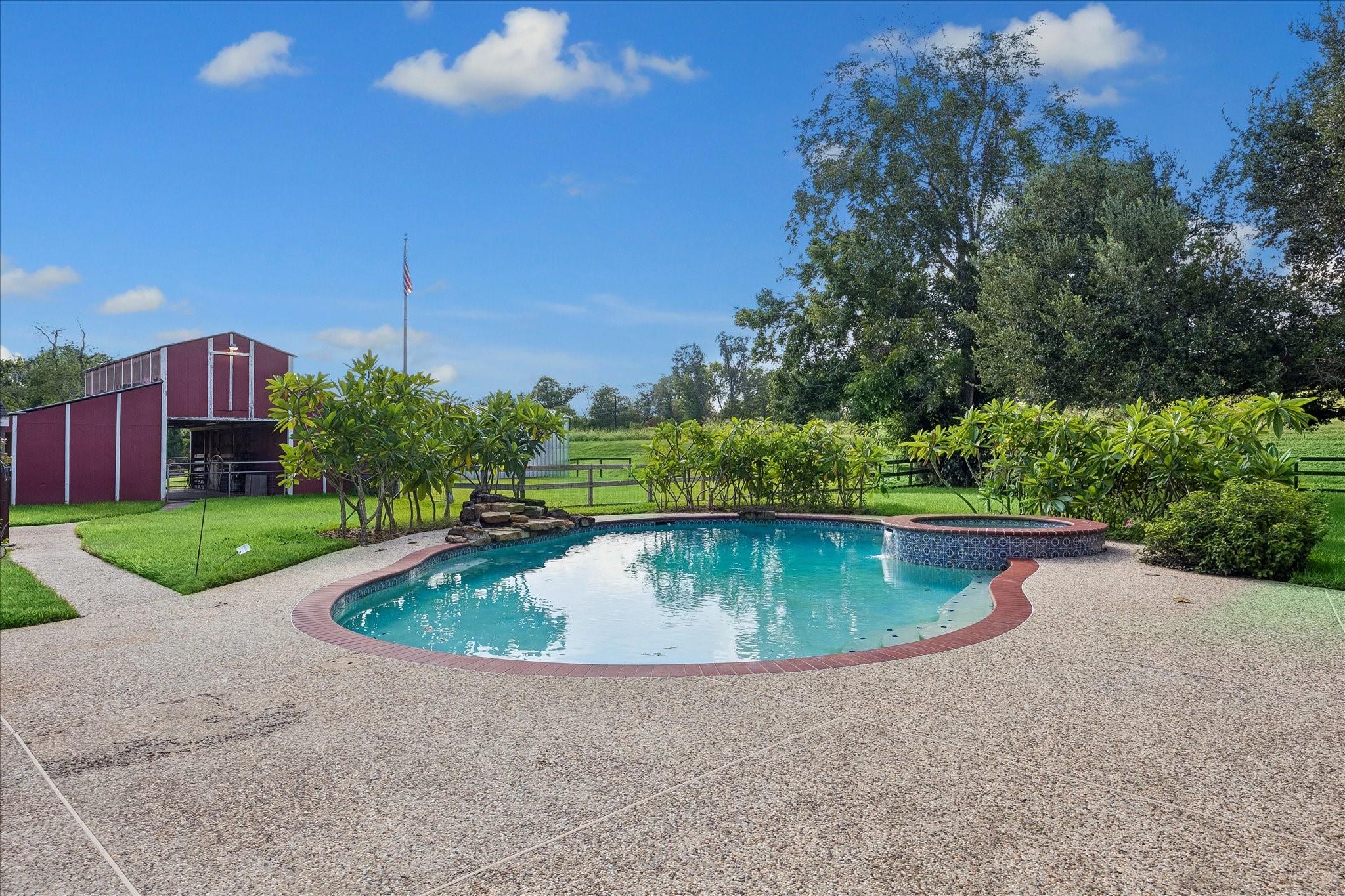 Backyard pool and raised spa beside a concrete deck, with a red barn in the background.