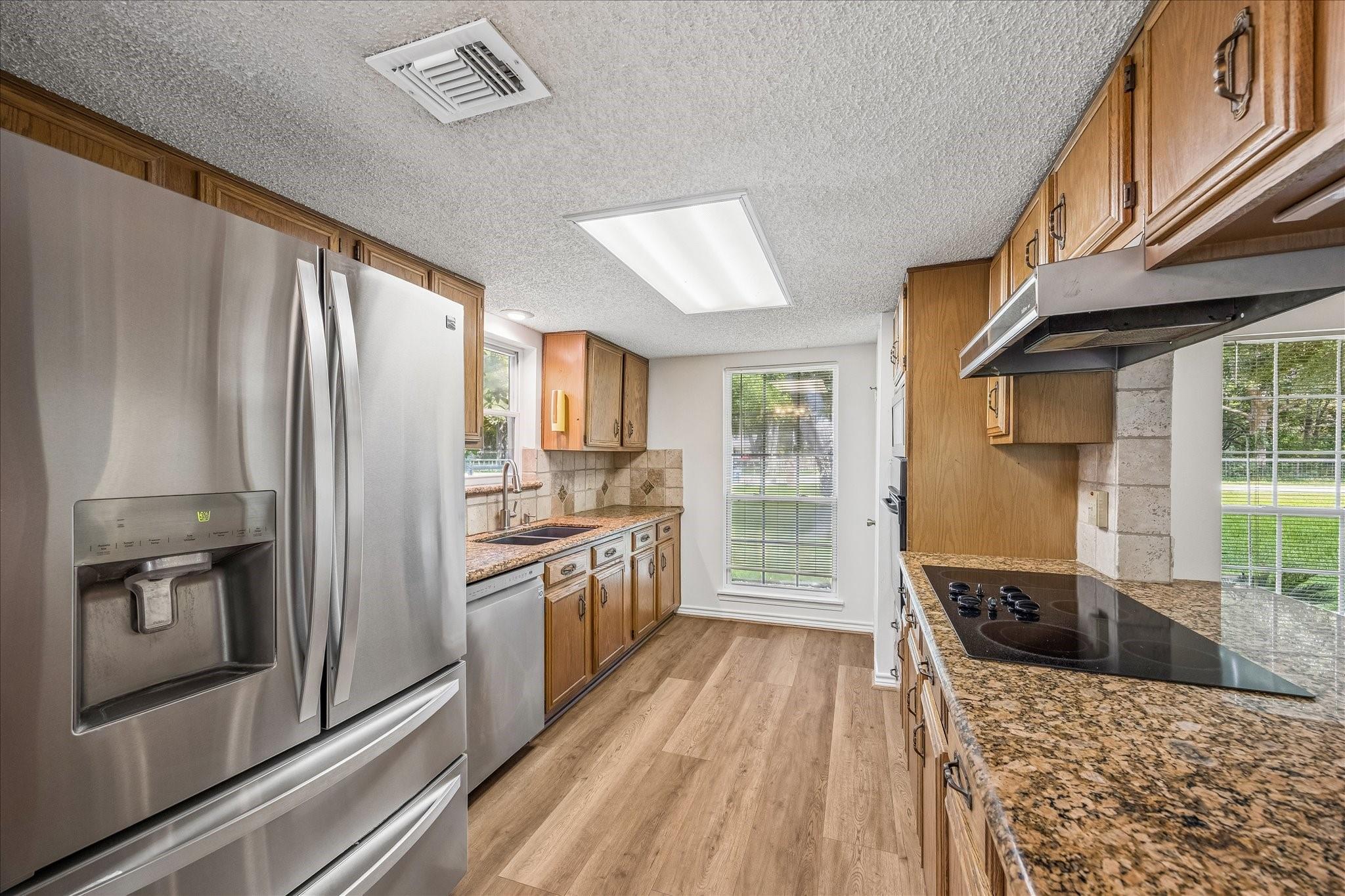 Kitchen with wood cabinets, granite counters, stainless steel refrigerator, and black cooktop.