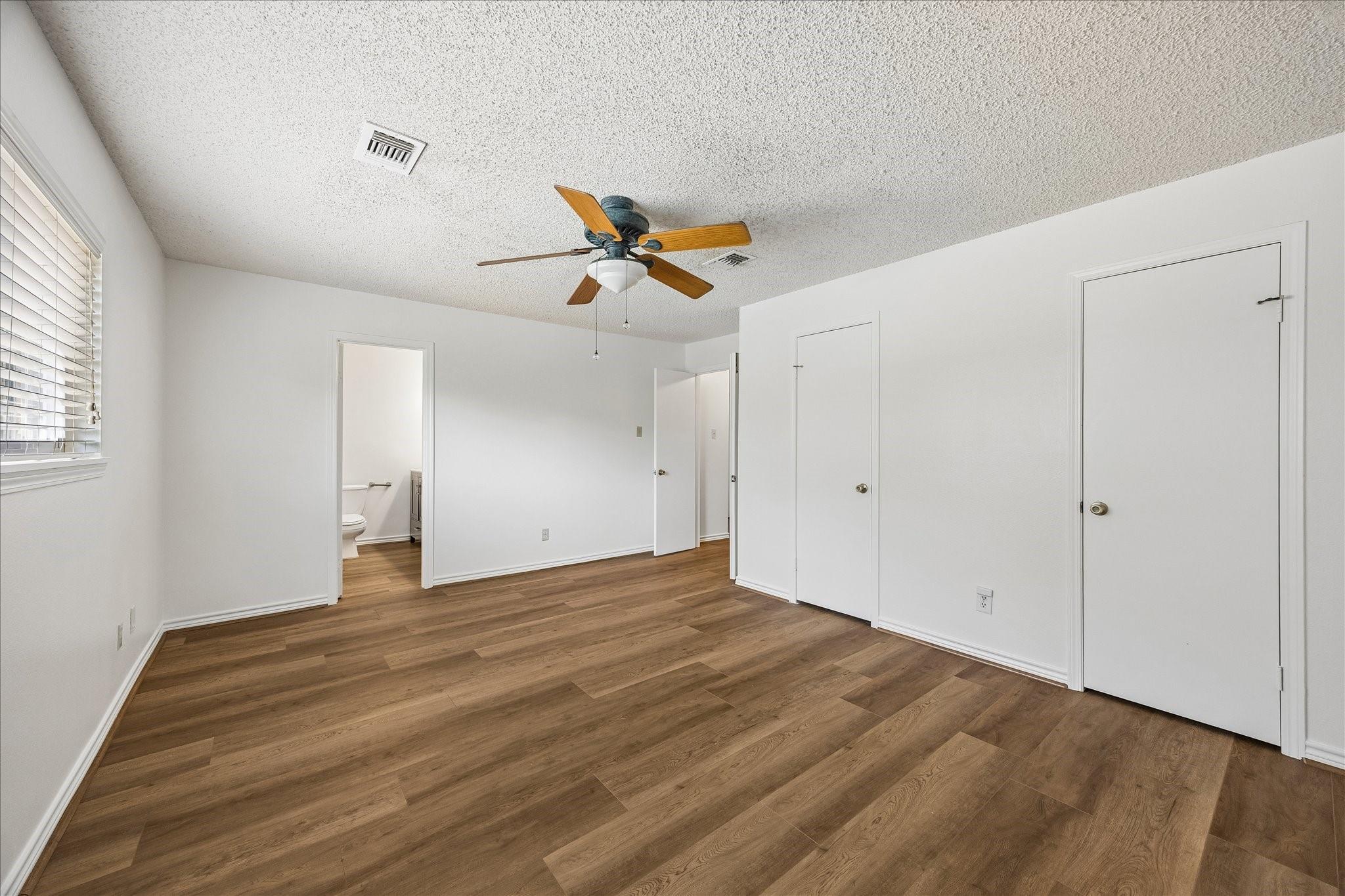 Unfurnished bedroom with wood-look floors, a ceiling fan, and a doorway to the bathroom.
