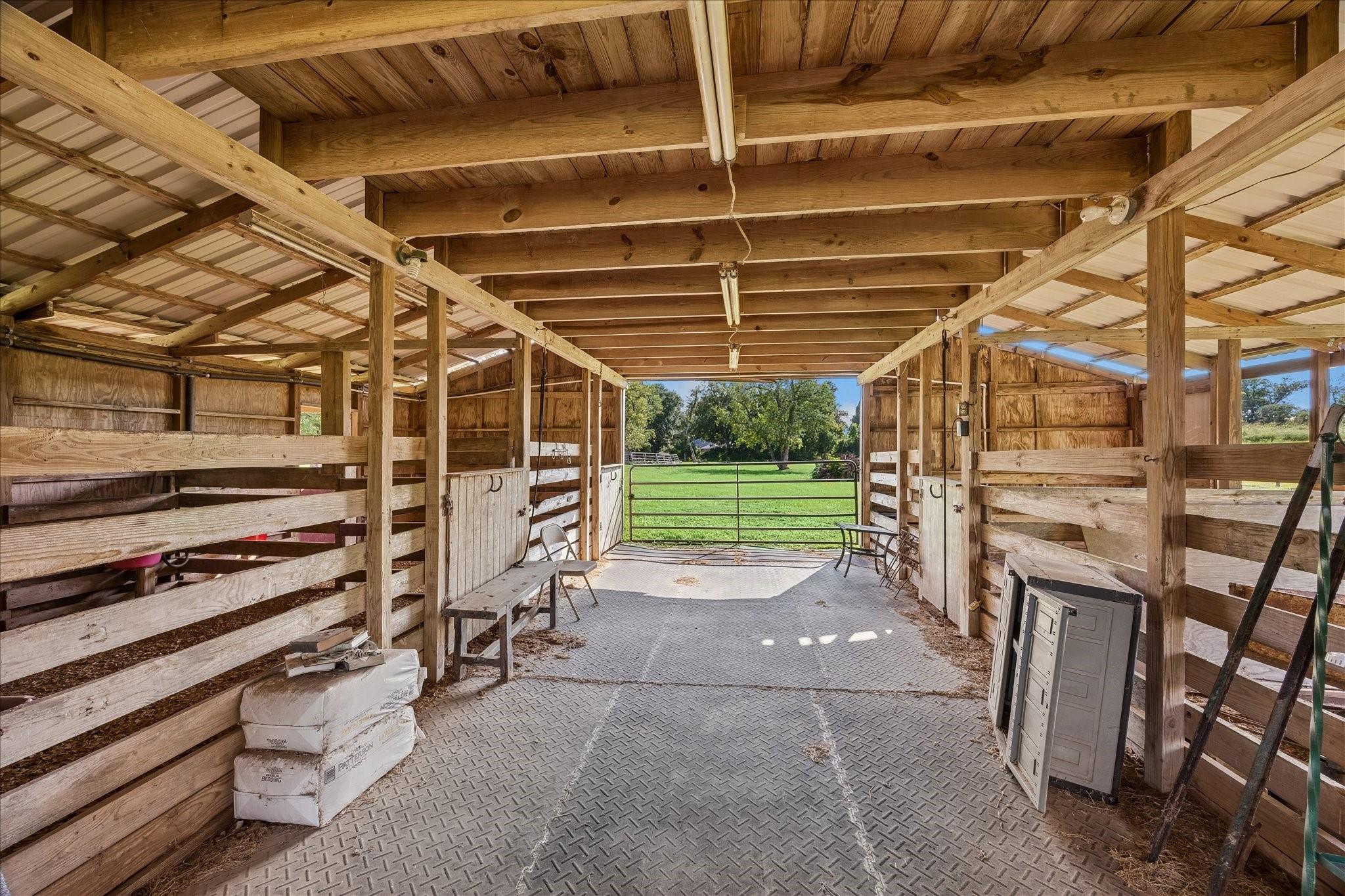 Wooden livestock barn with divided stalls, a metal floor, and open pasture beyond.