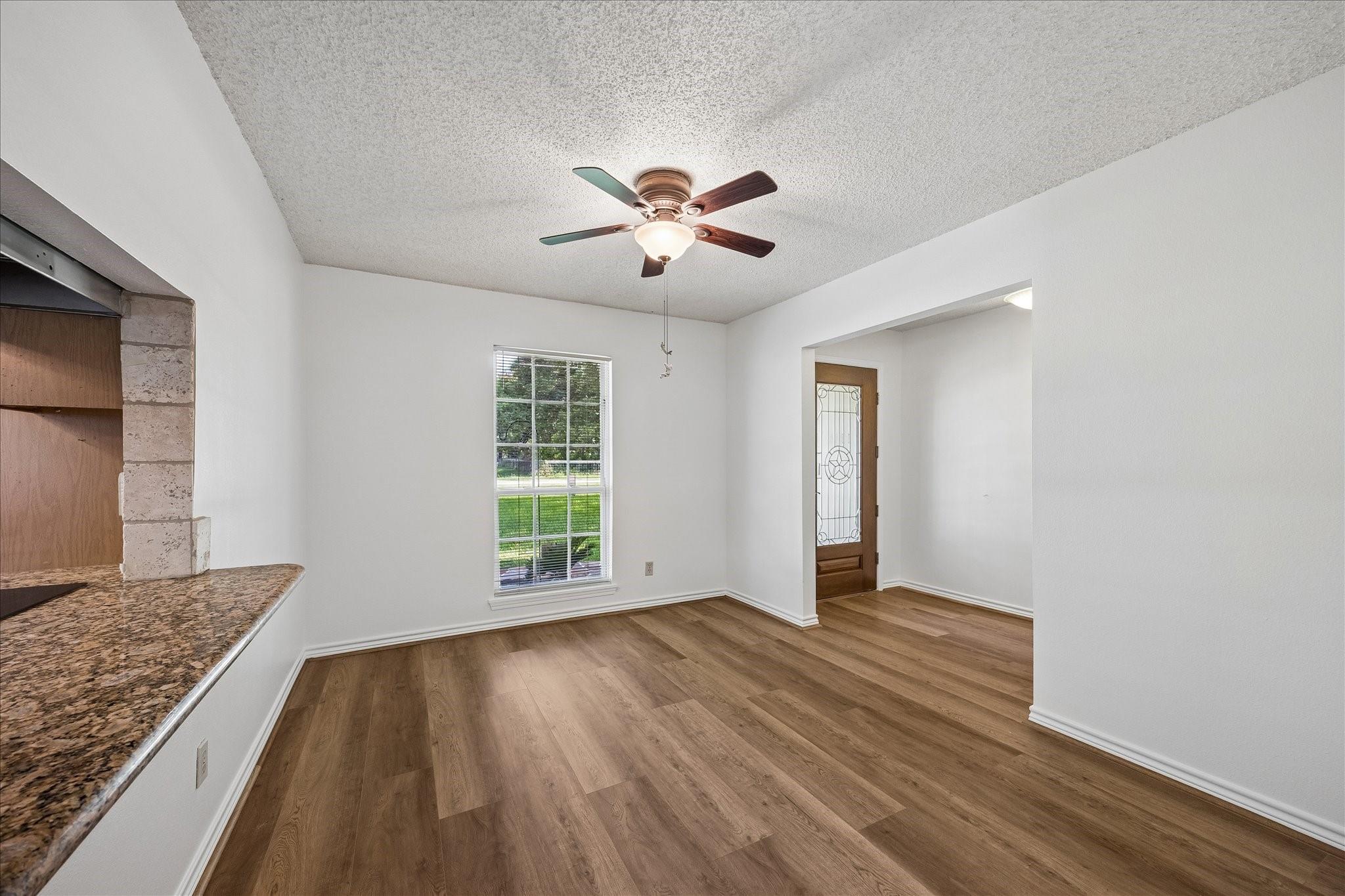 Empty room with wood-look flooring, a ceiling fan, window, and granite counter edge.