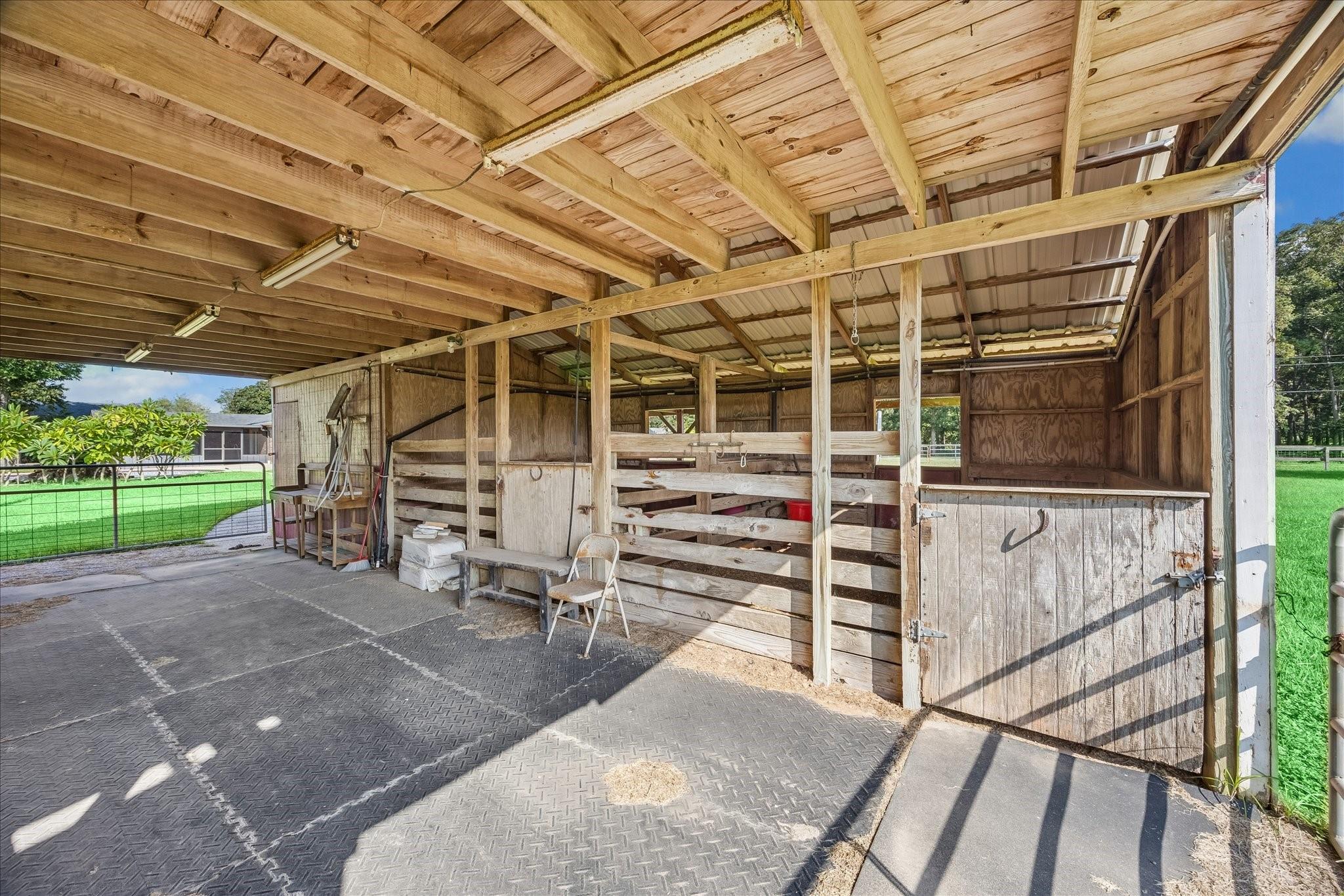 Open-sided wooden horse stable with divided stalls and a covered grooming area.