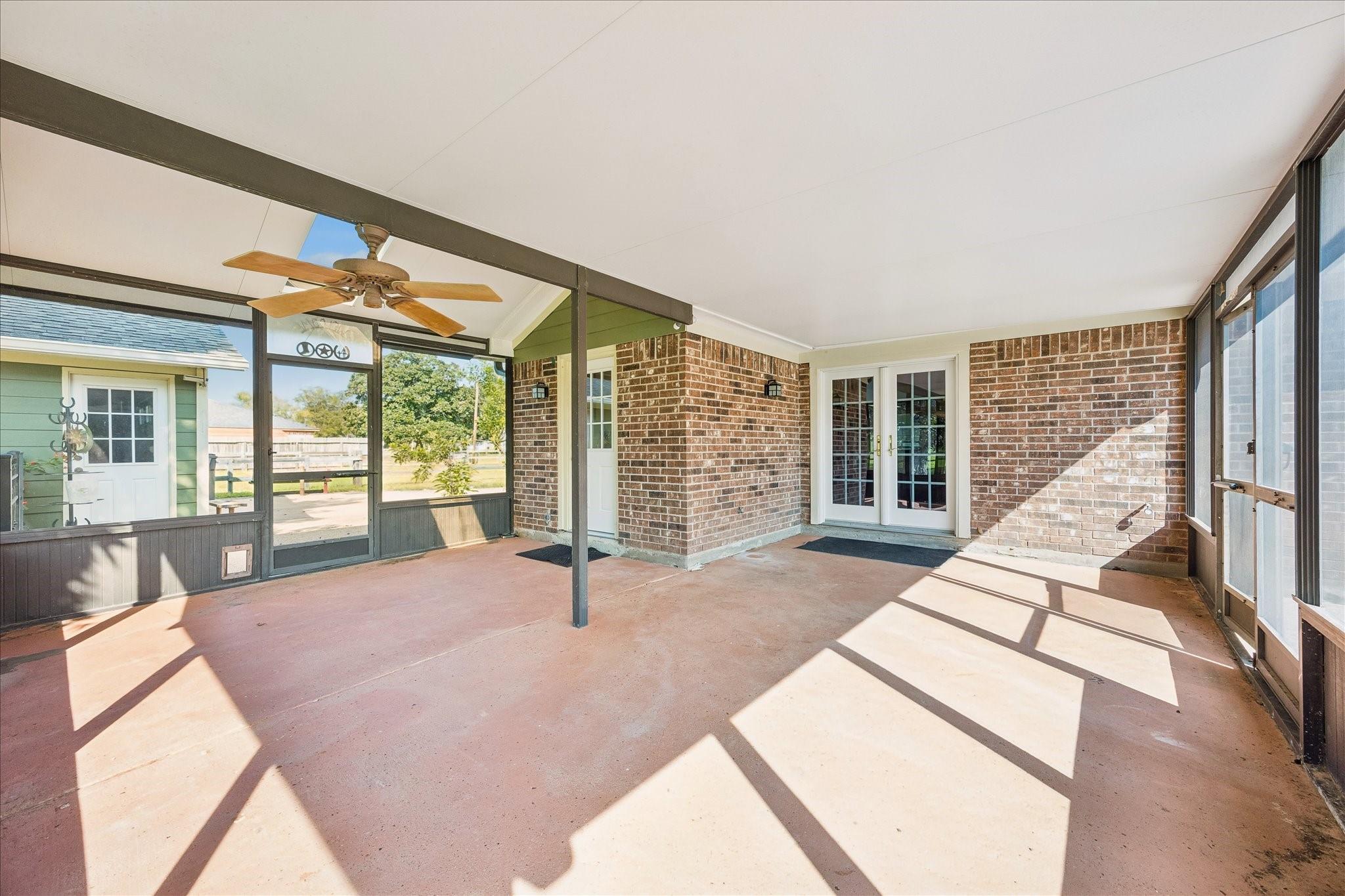 Screened-in patio with a ceiling fan, brick walls, and French doors.