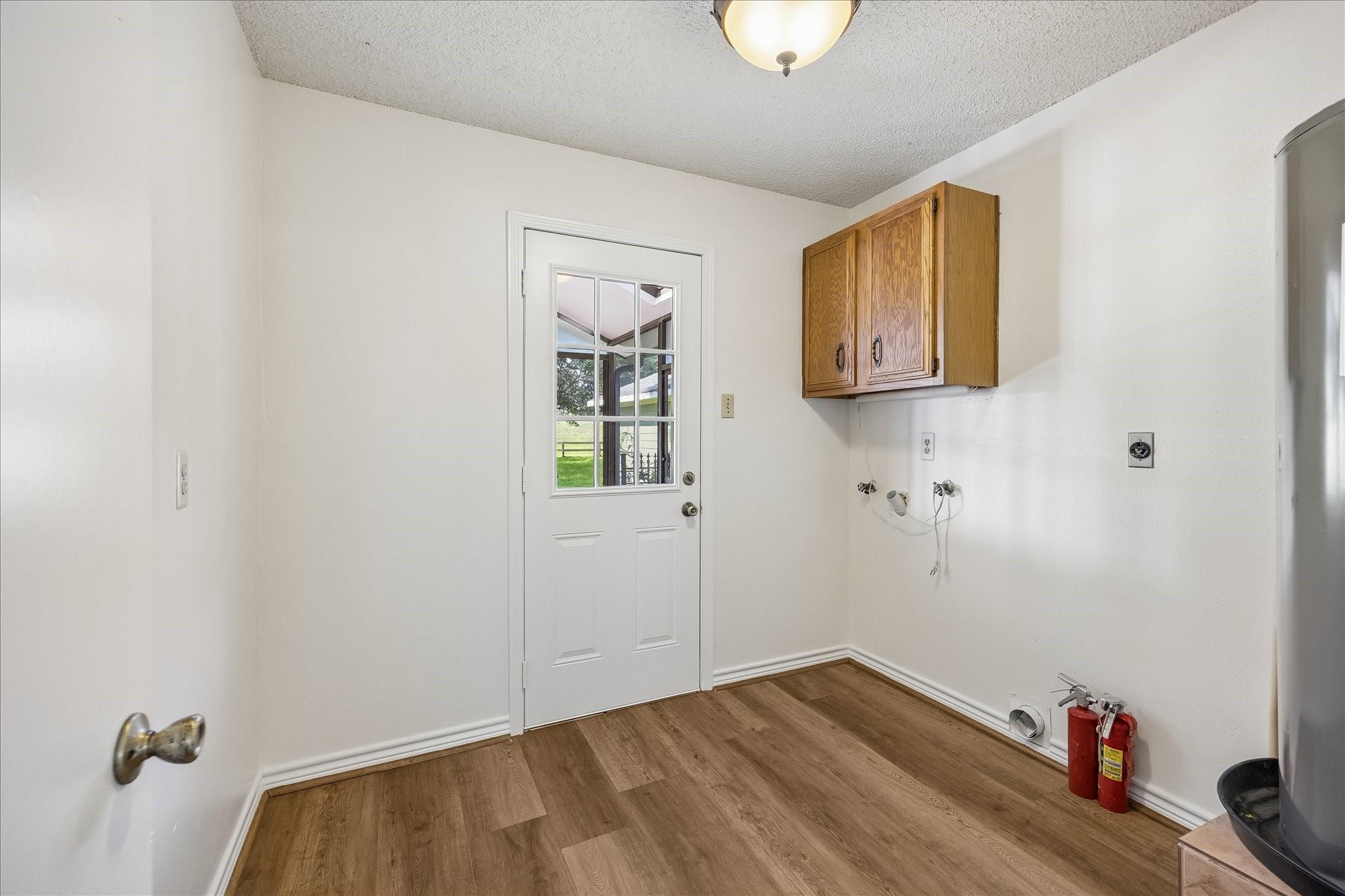 Vacant utility room with wooden cabinets, laundry hookups, and a windowed exterior door.